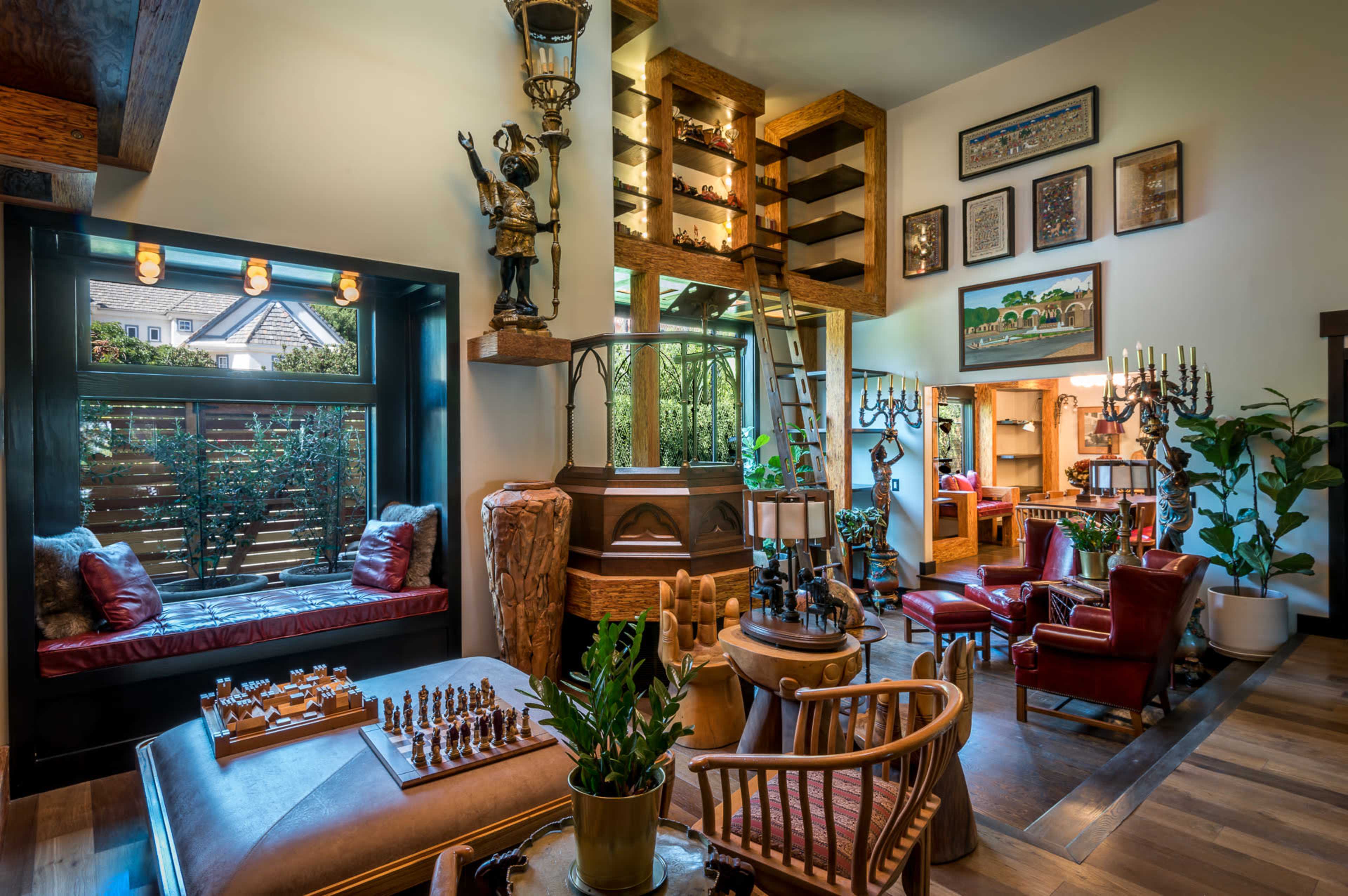 A cozy indoor space featuring a chess set, a large wooden shelf filled with decorative items, and comfortable seating arranged around plants and warm lighting.