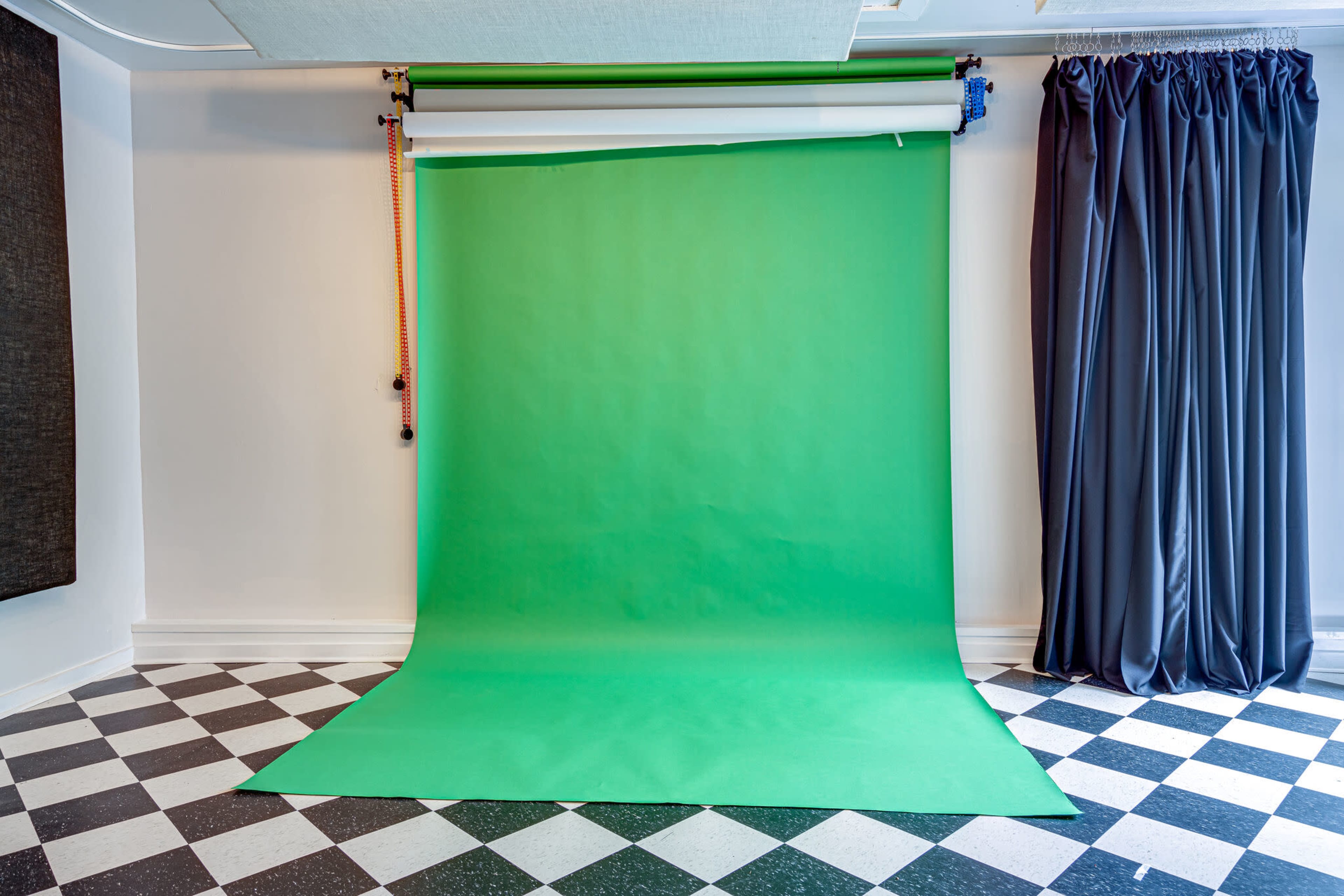 A green screen studio setup with a green backdrop and black and white checkered flooring.