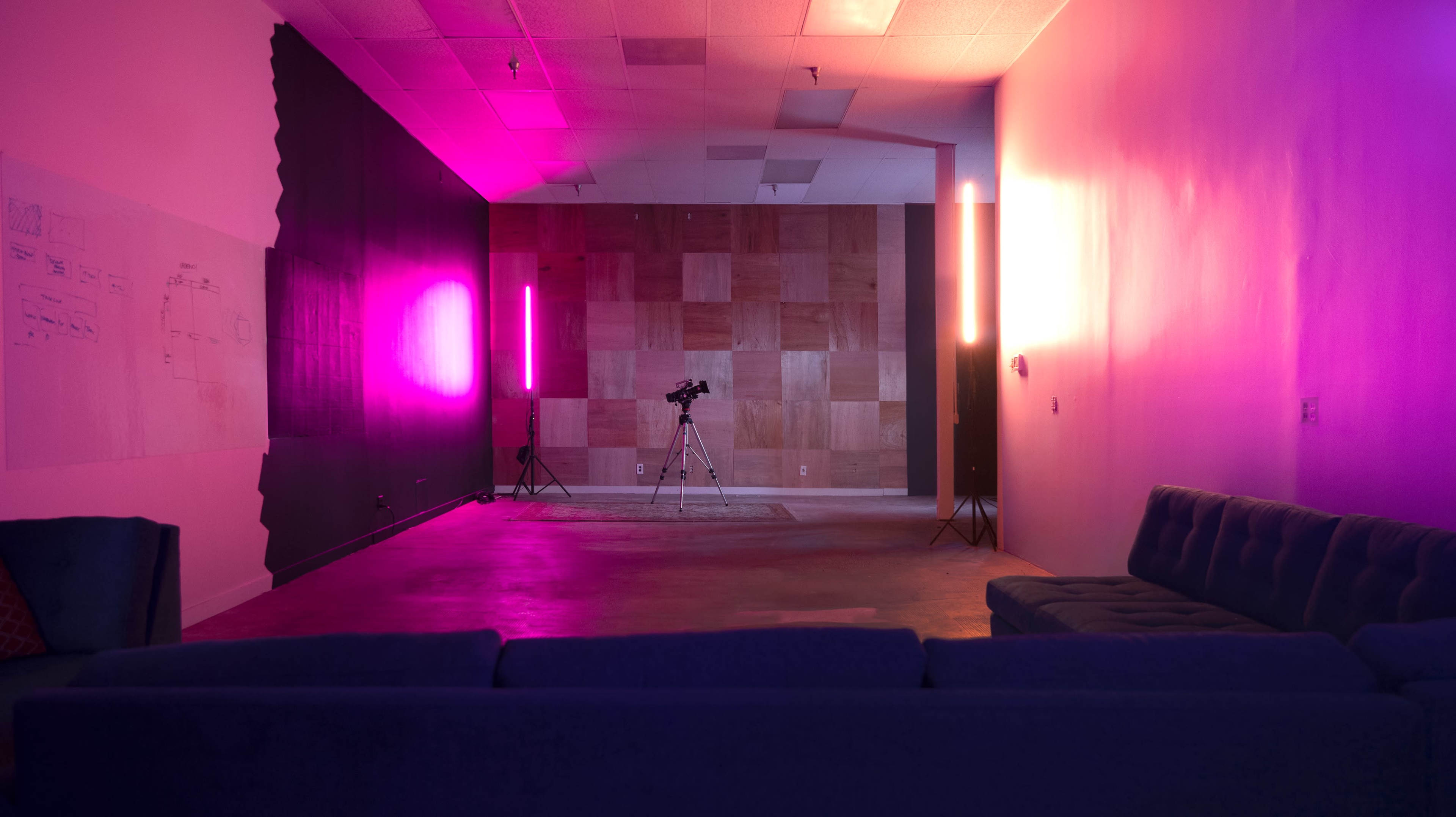 A spacious room with a wood-paneled wall, a tripod in the center, and colored lighting creating a gradient effect on the walls.