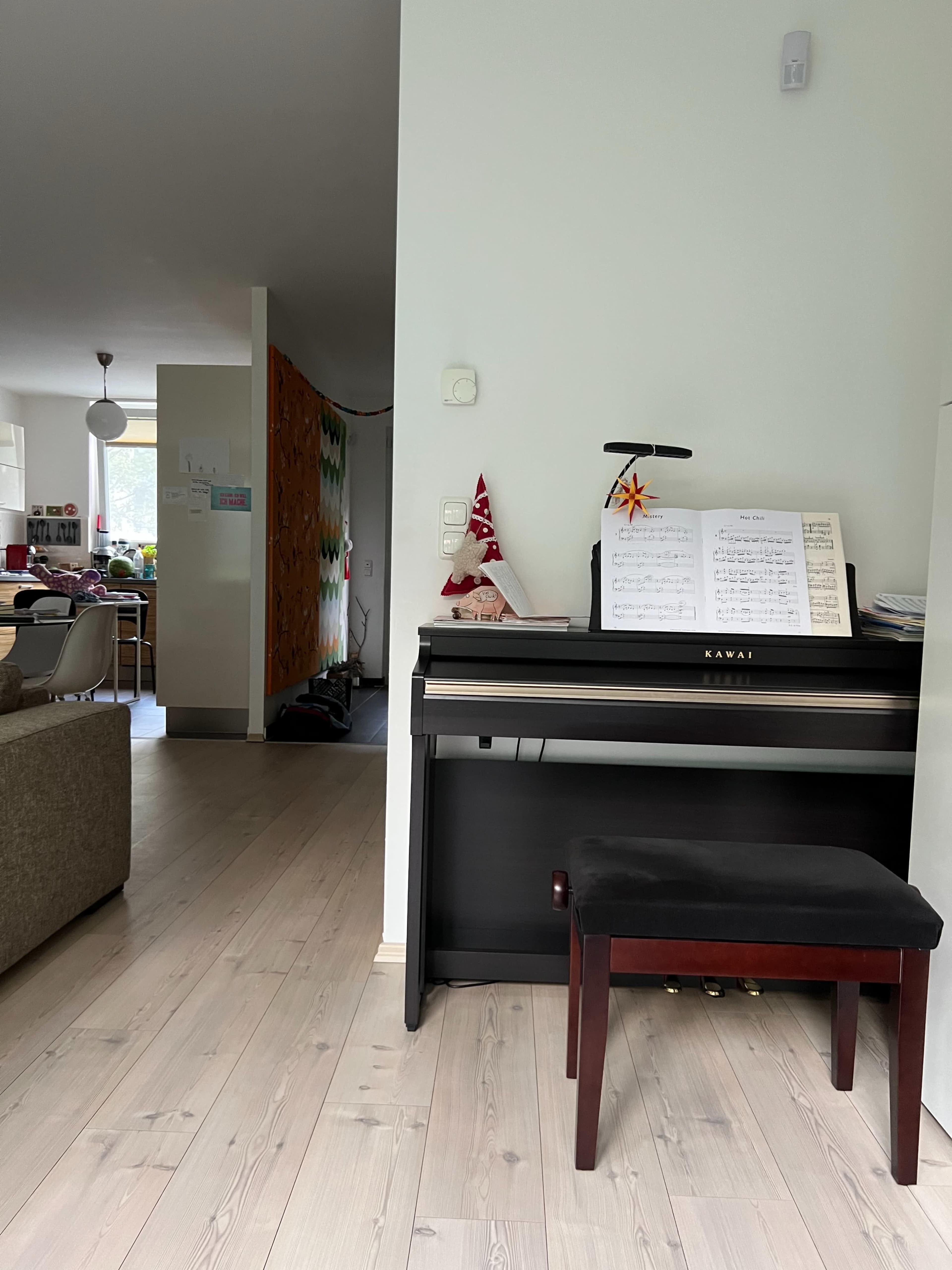 A black digital piano with sheet music and a stand is placed against a light-colored wall in a spacious, modern room.