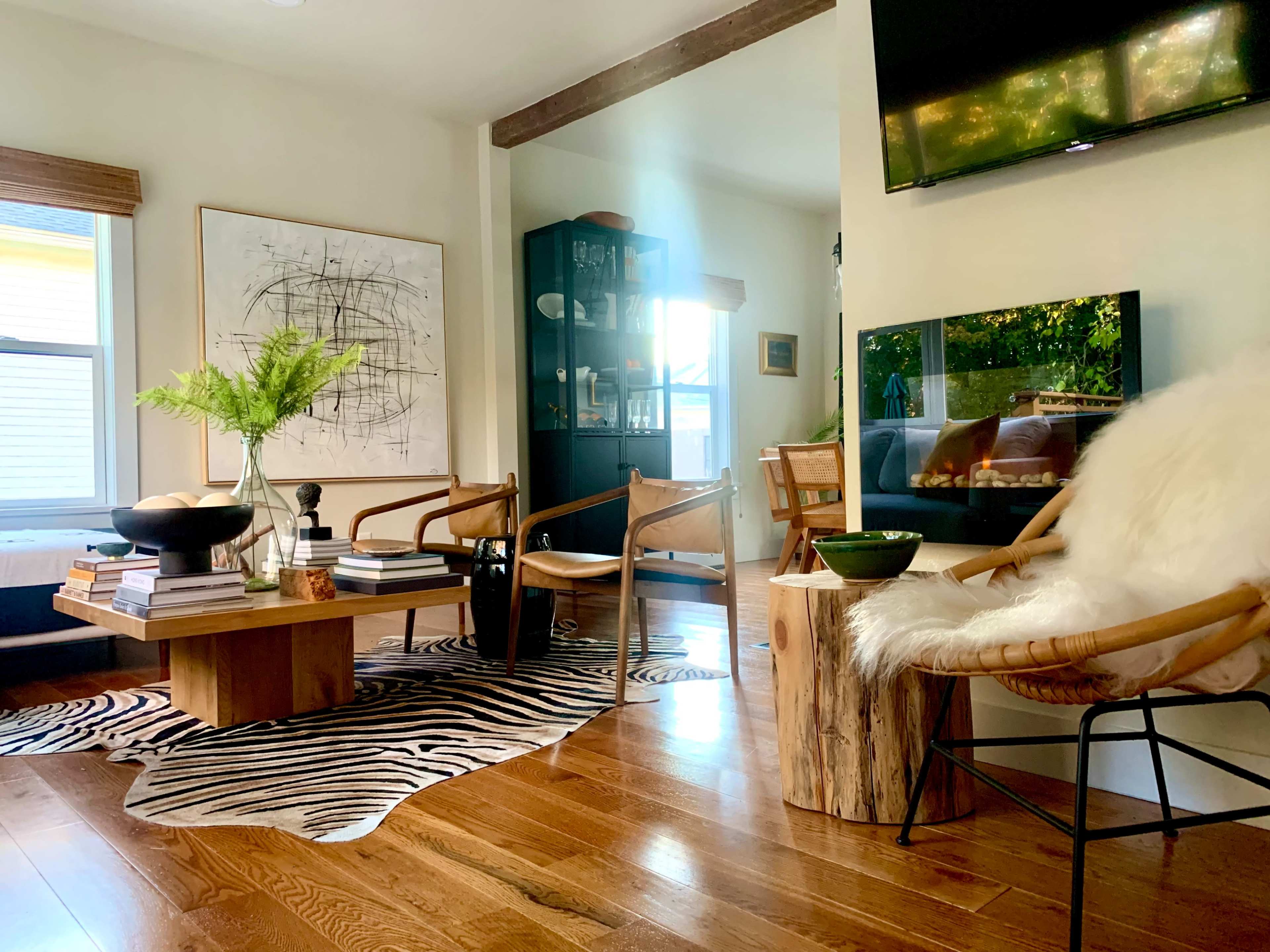 A modern living room features a wooden table, two chairs, a black display cabinet, and a television, with a zebra-patterned rug on the floor.