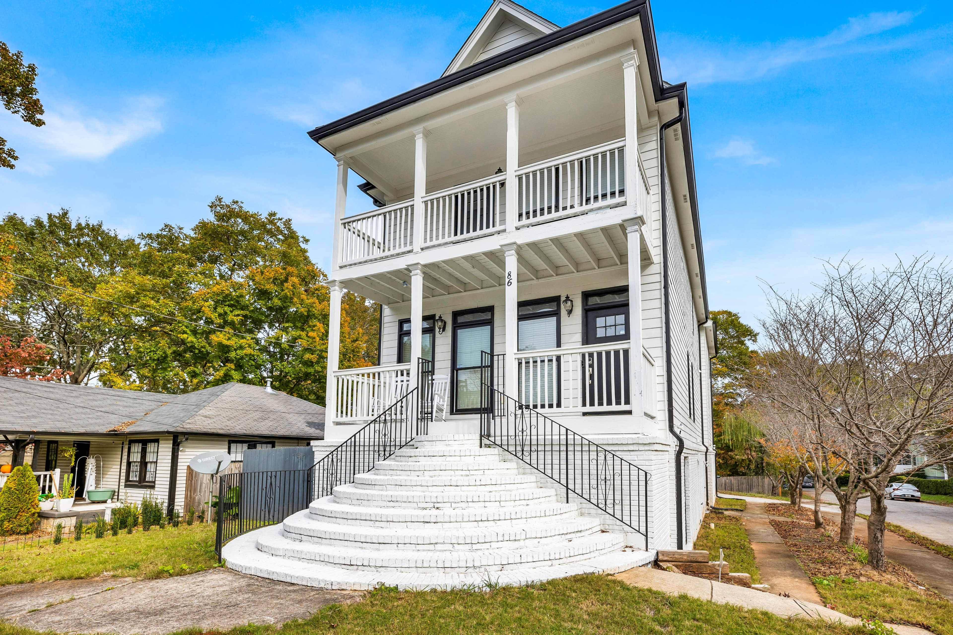 A large, white two-story house with a spacious front staircase and two balconies on the upper level.
