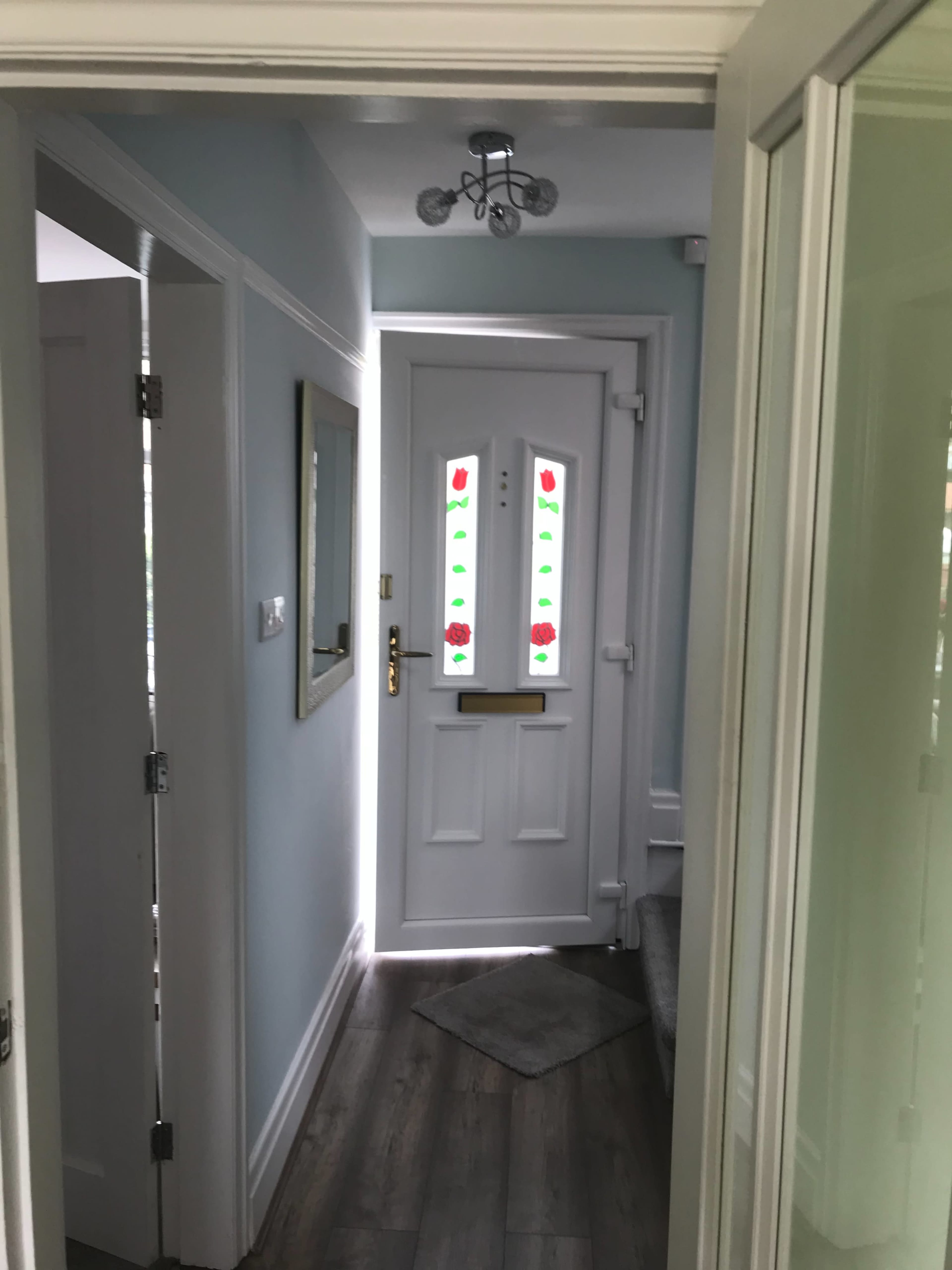 A hallway with a white front door featuring colorful glass panels, leading to a light-colored room.