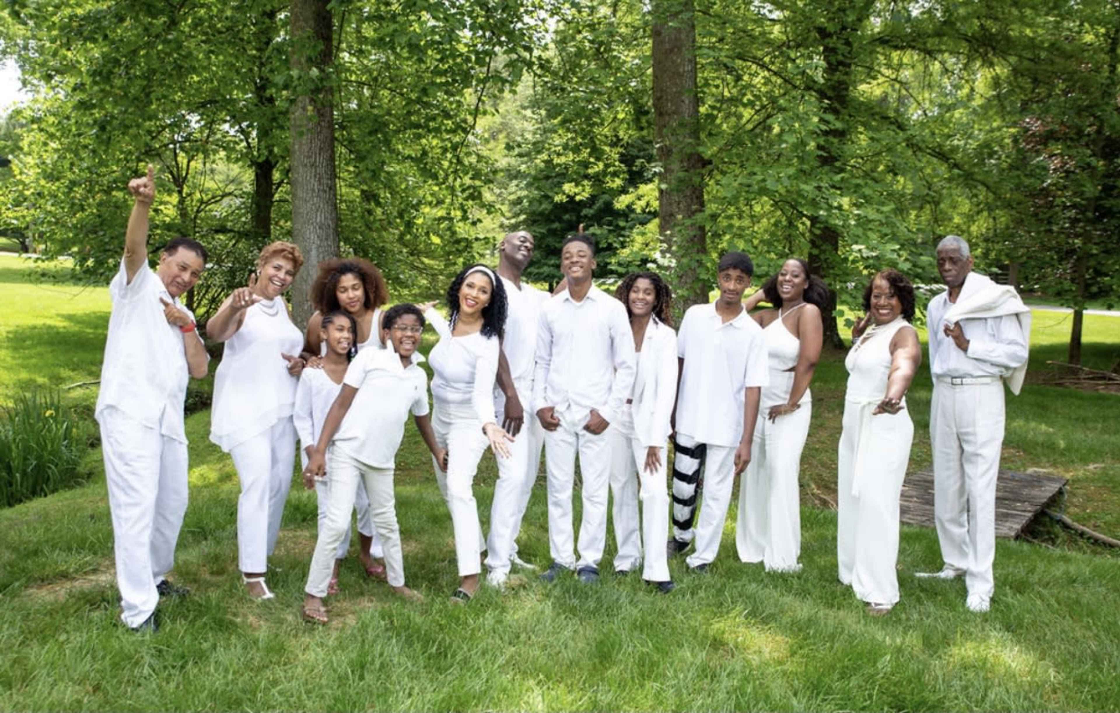 A group of people dressed in white clothing stands together in a green outdoor setting, smiling and posing for a photo.