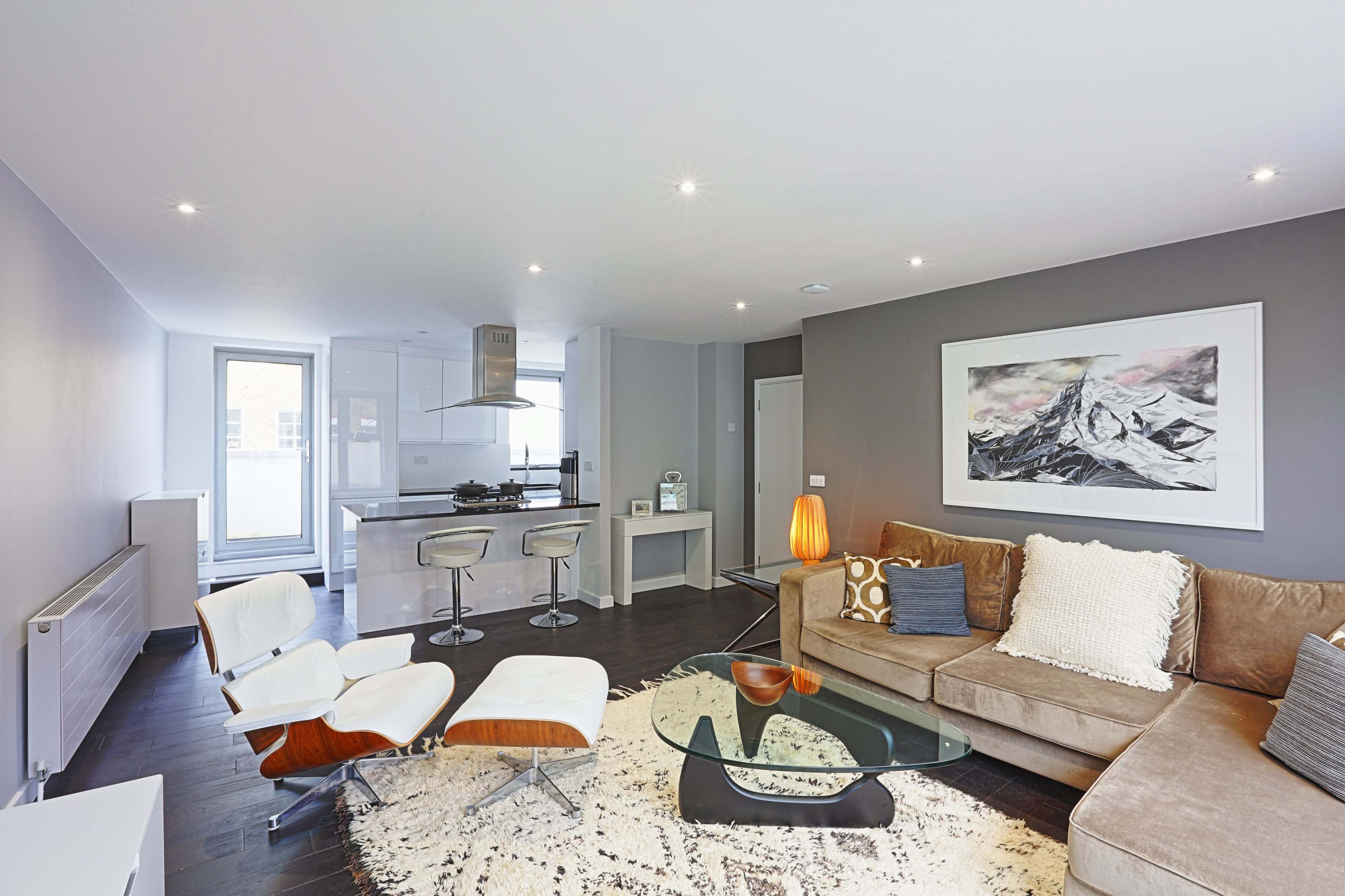 A modern living room with a sectional sofa, a glass coffee table, and an open kitchen area featuring a breakfast bar and stylish appliances.