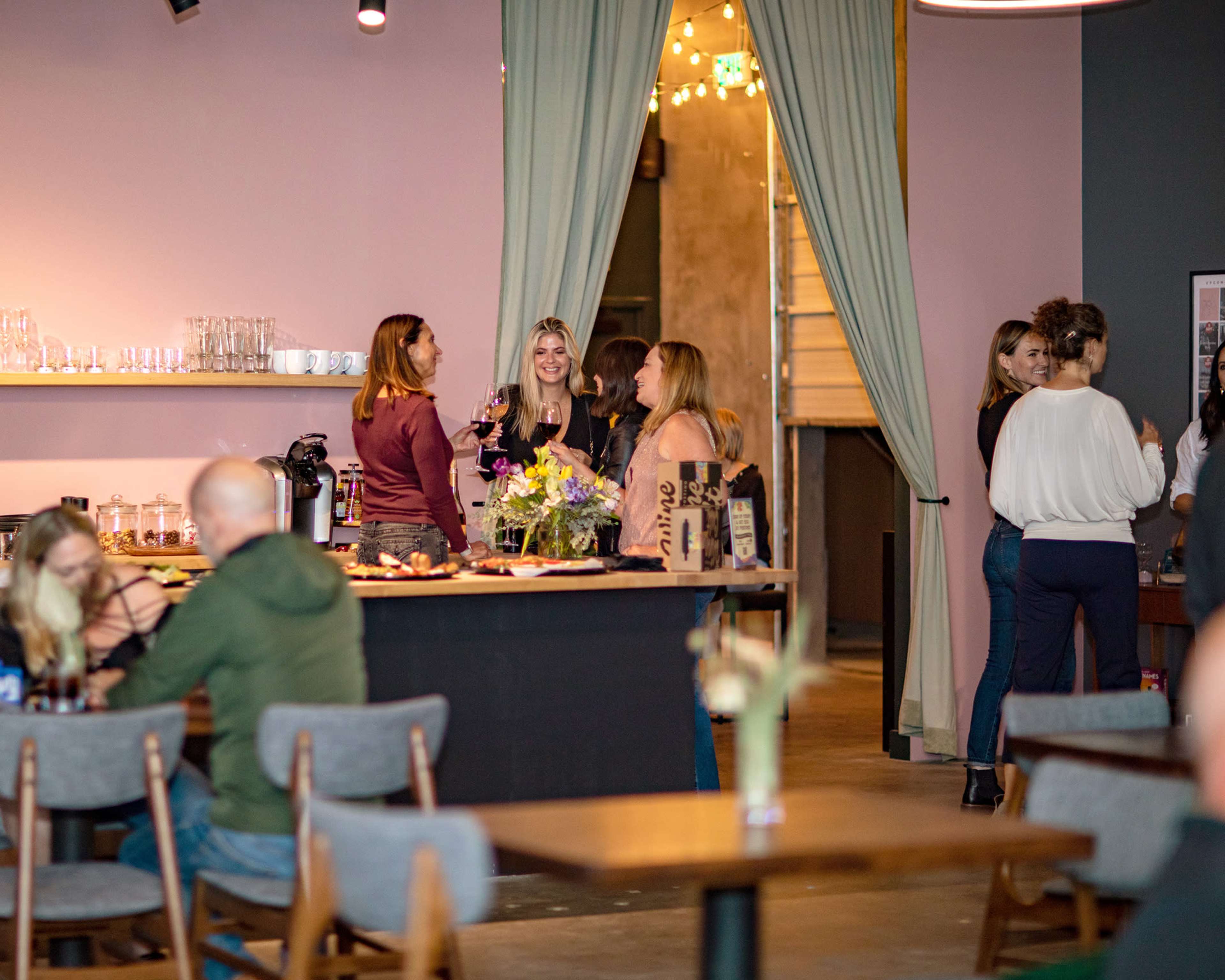 A group of people socializes near a bar area in a modern interior space with floral arrangements and soft lighting.