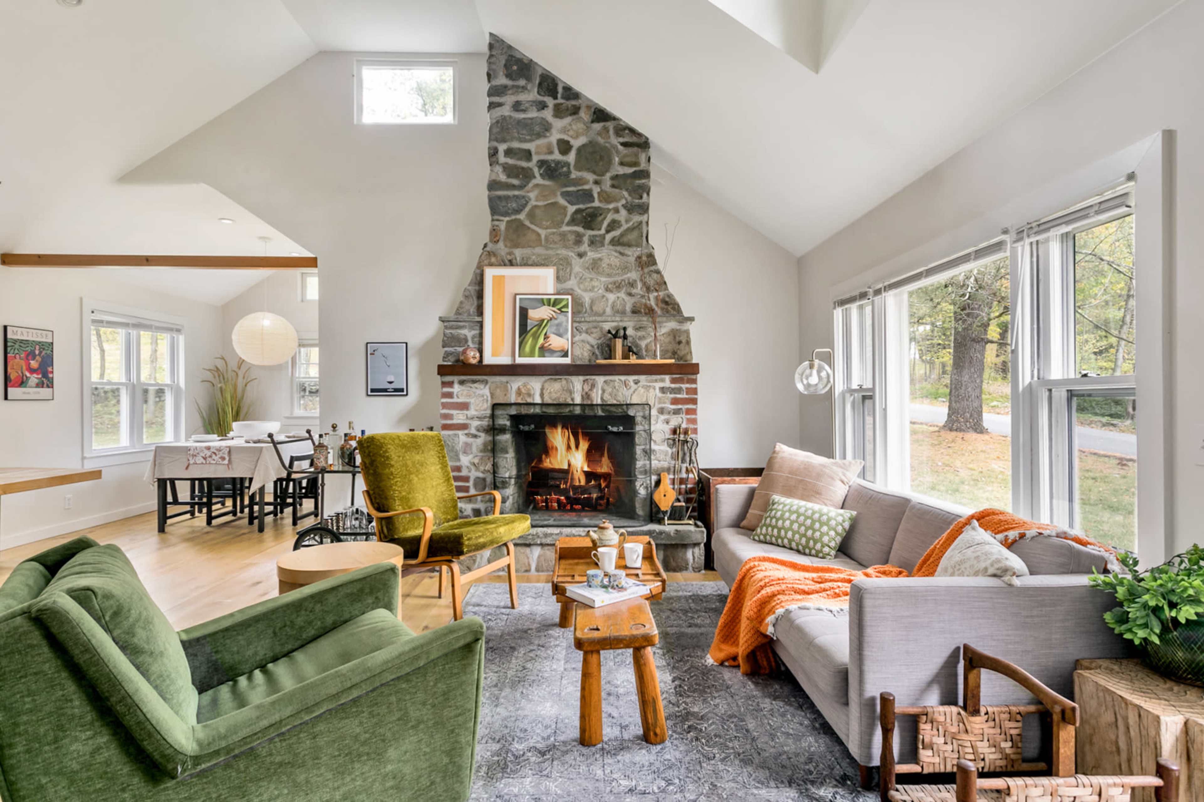 A cozy living room features a stone fireplace surrounded by comfortable seating, with large windows allowing natural light to illuminate the space.