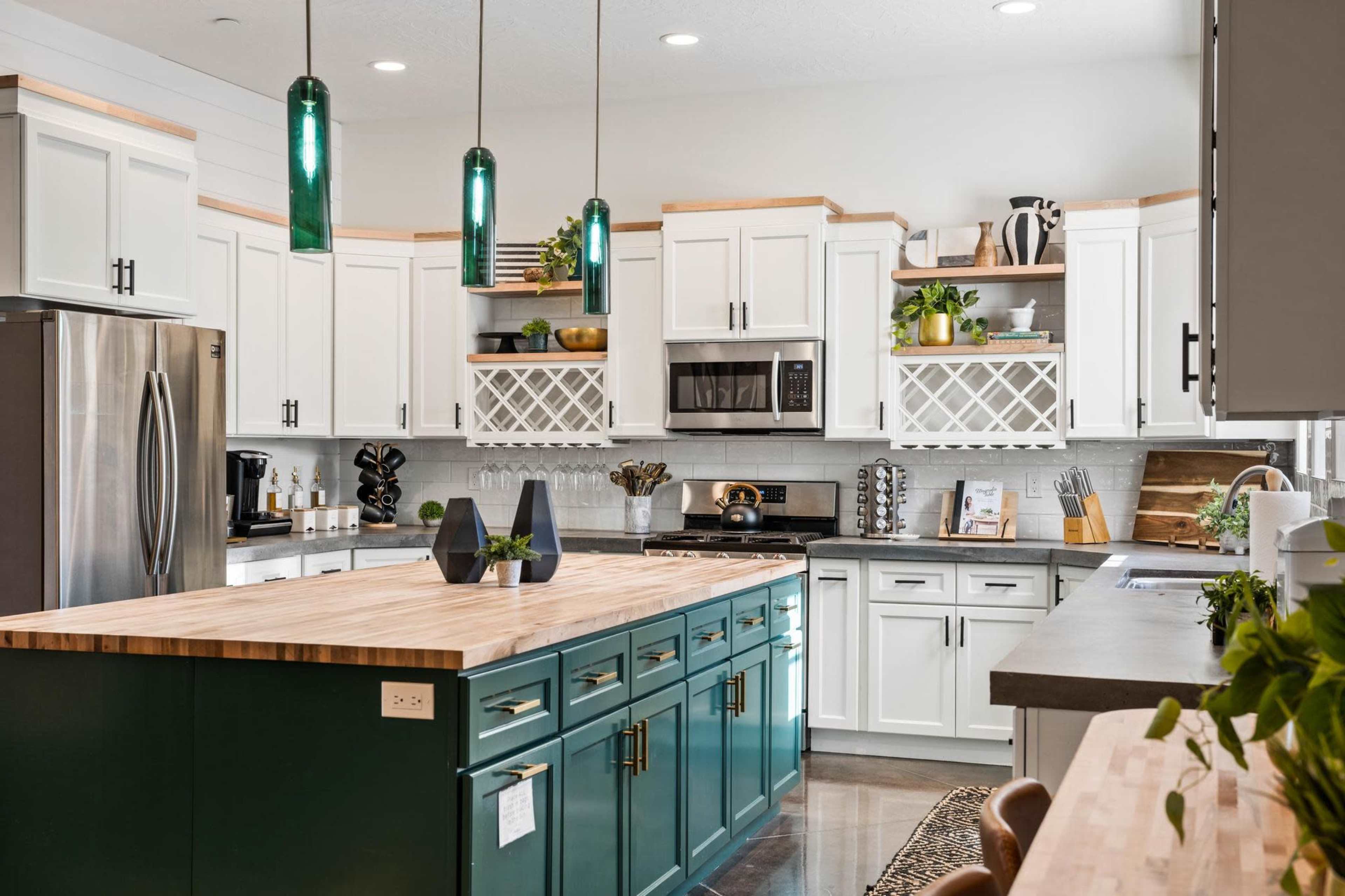 A modern kitchen features white cabinetry, a large wooden island with green accents, and stainless steel appliances.