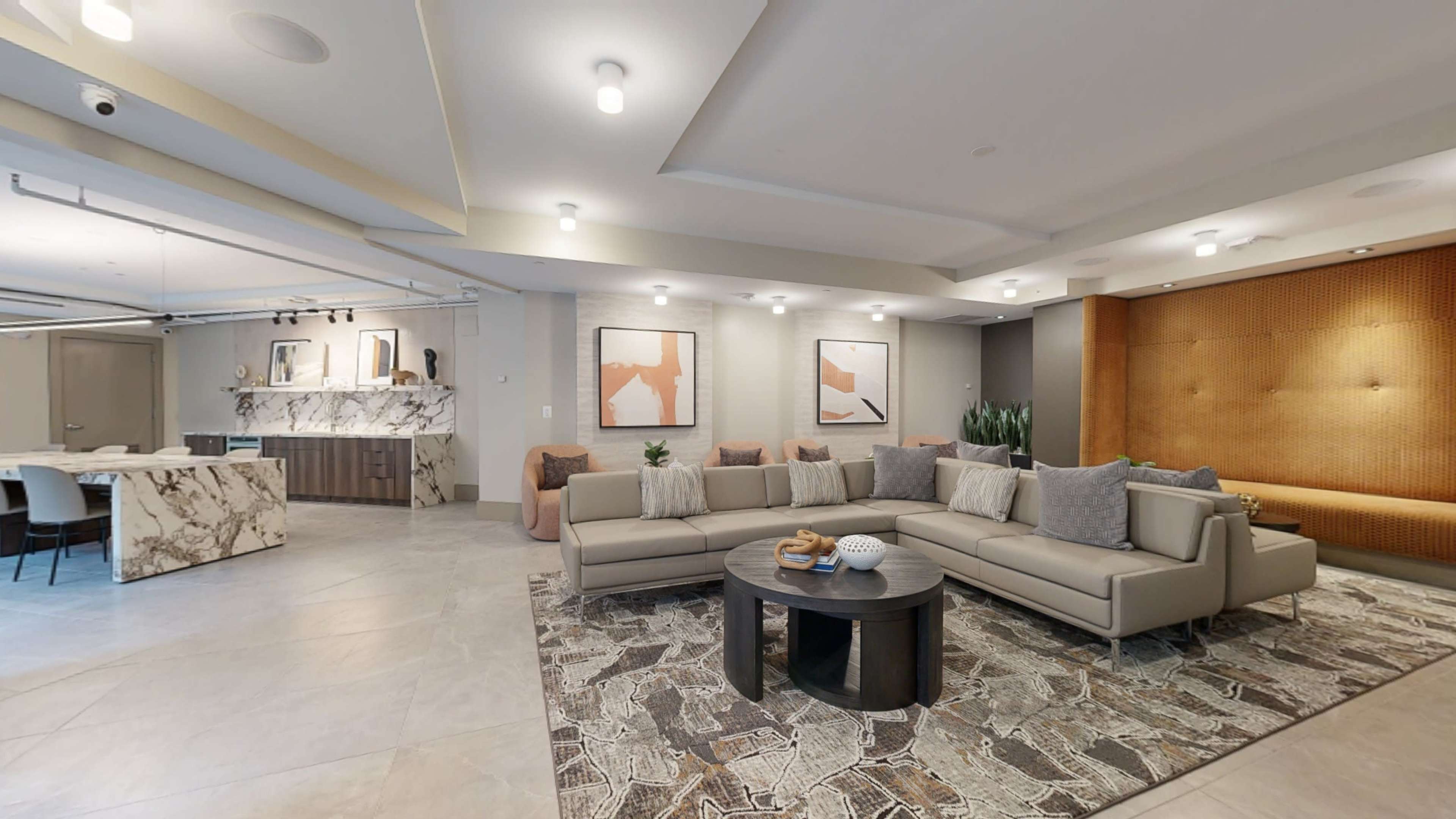 A modern living room with a sectional sofa, a circular coffee table, and artwork on the walls, leading to an open kitchen area.