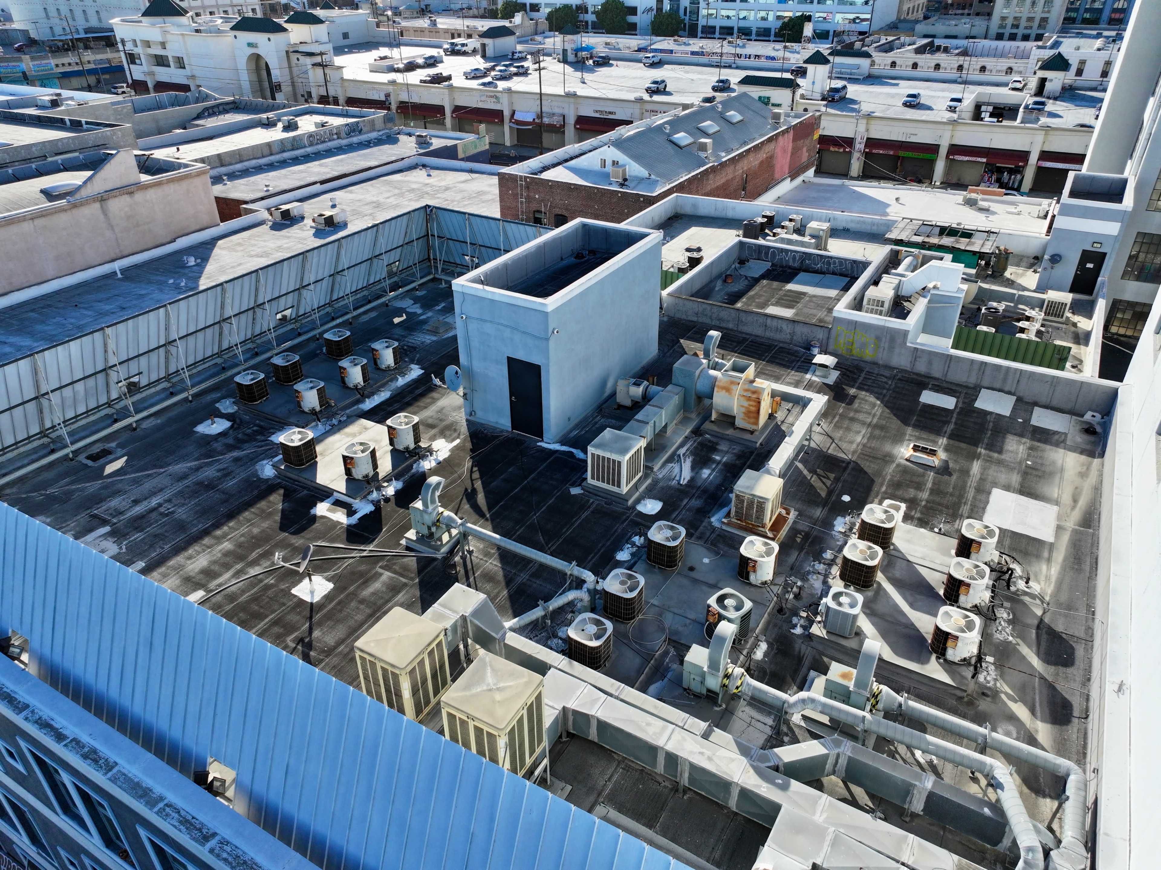 A flat rooftop covered with various air conditioning units and ventilation equipment, surrounded by buildings in an urban area.