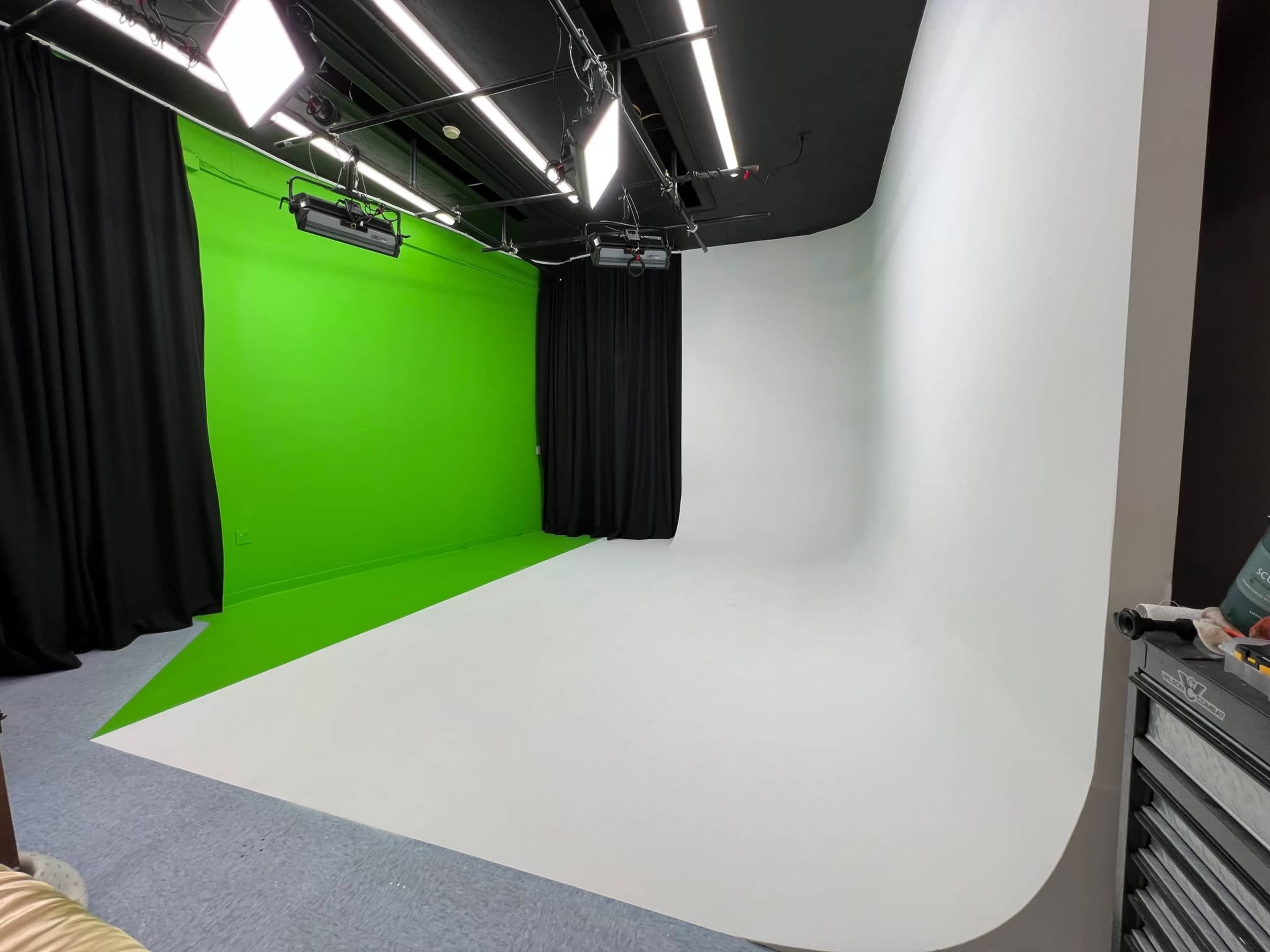 A photography studio featuring a green screen on one side and a white seamless backdrop on the other, with lights and curtains around the space.