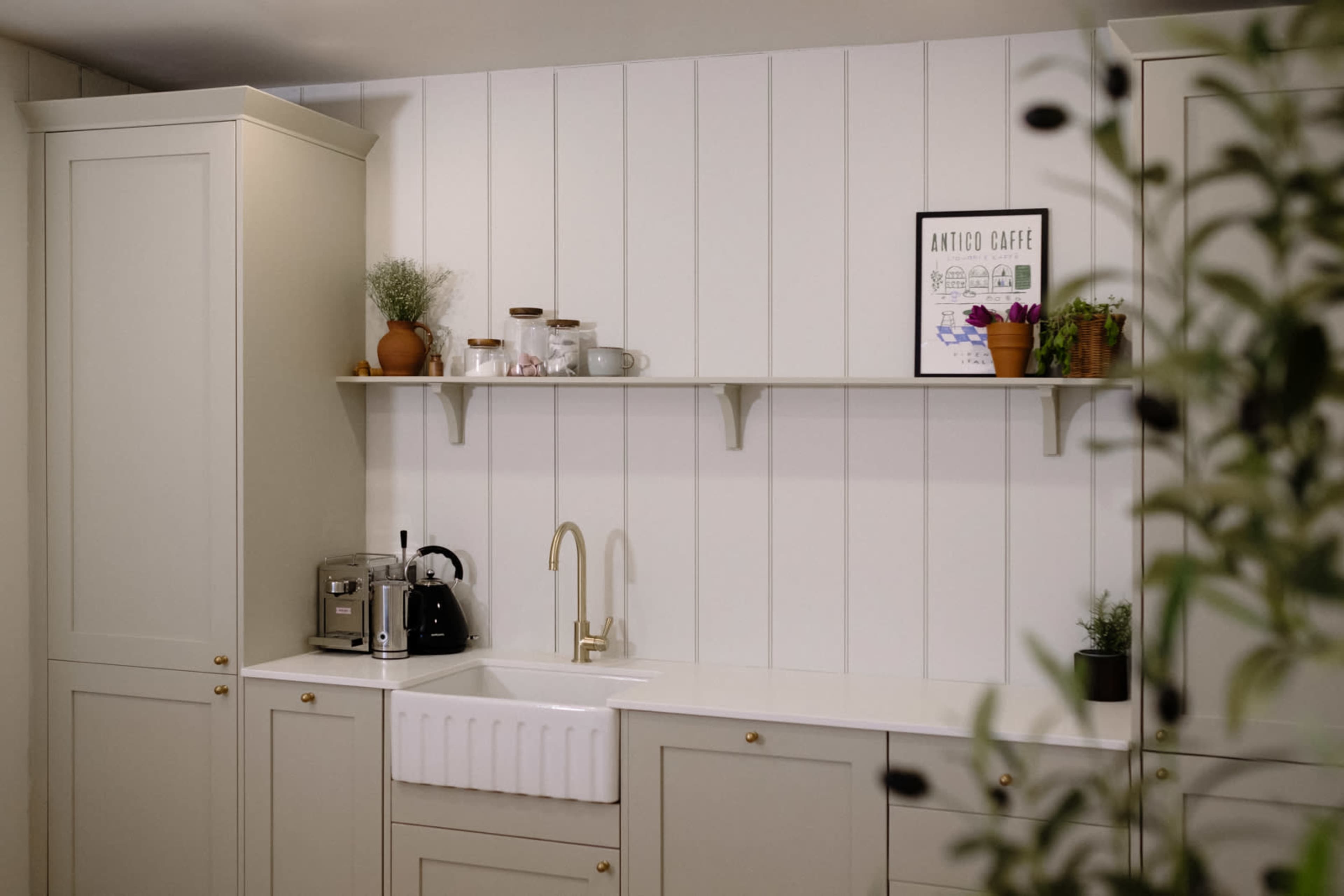 A modern kitchen featuring a classic farmhouse sink, cabinetry, and a minimalistic shelf with decorative plants and kitchenware.