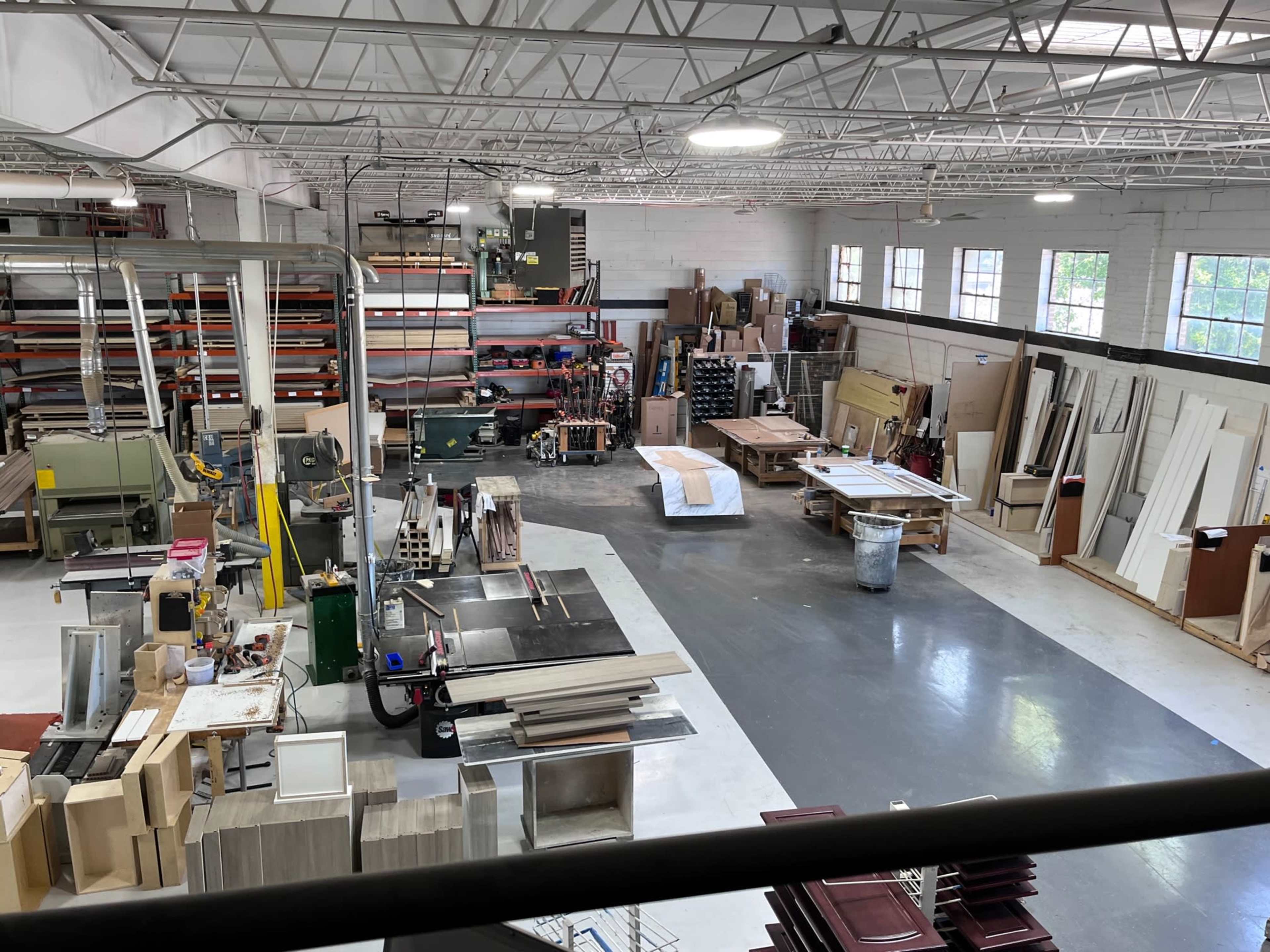 A spacious workshop filled with various woodworking equipment, materials, and finished products arranged on the floor.