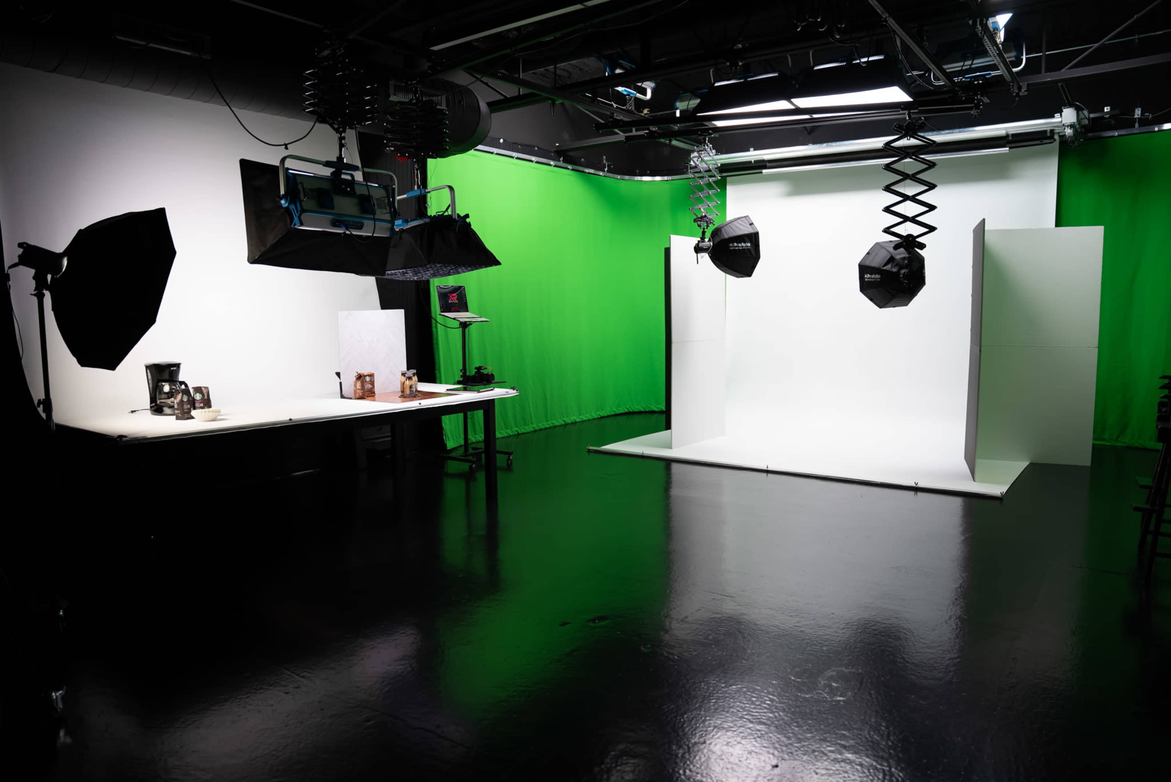 A photography studio features a green backdrop, a white backdrop, and various lighting equipment on a reflective floor.