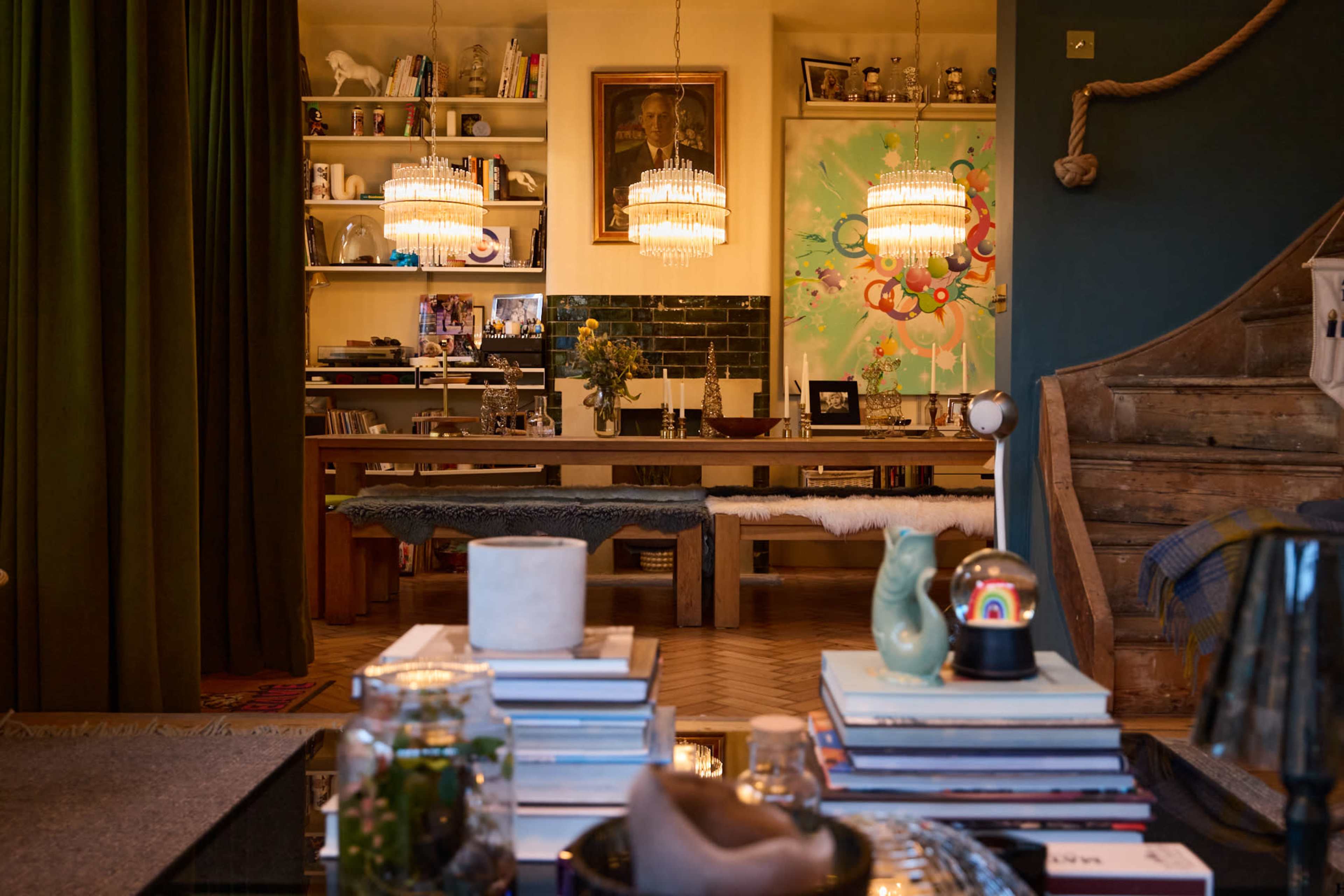 A contemporary living space features a wooden dining table, modern art on the walls, and shelves filled with books and decorative items.