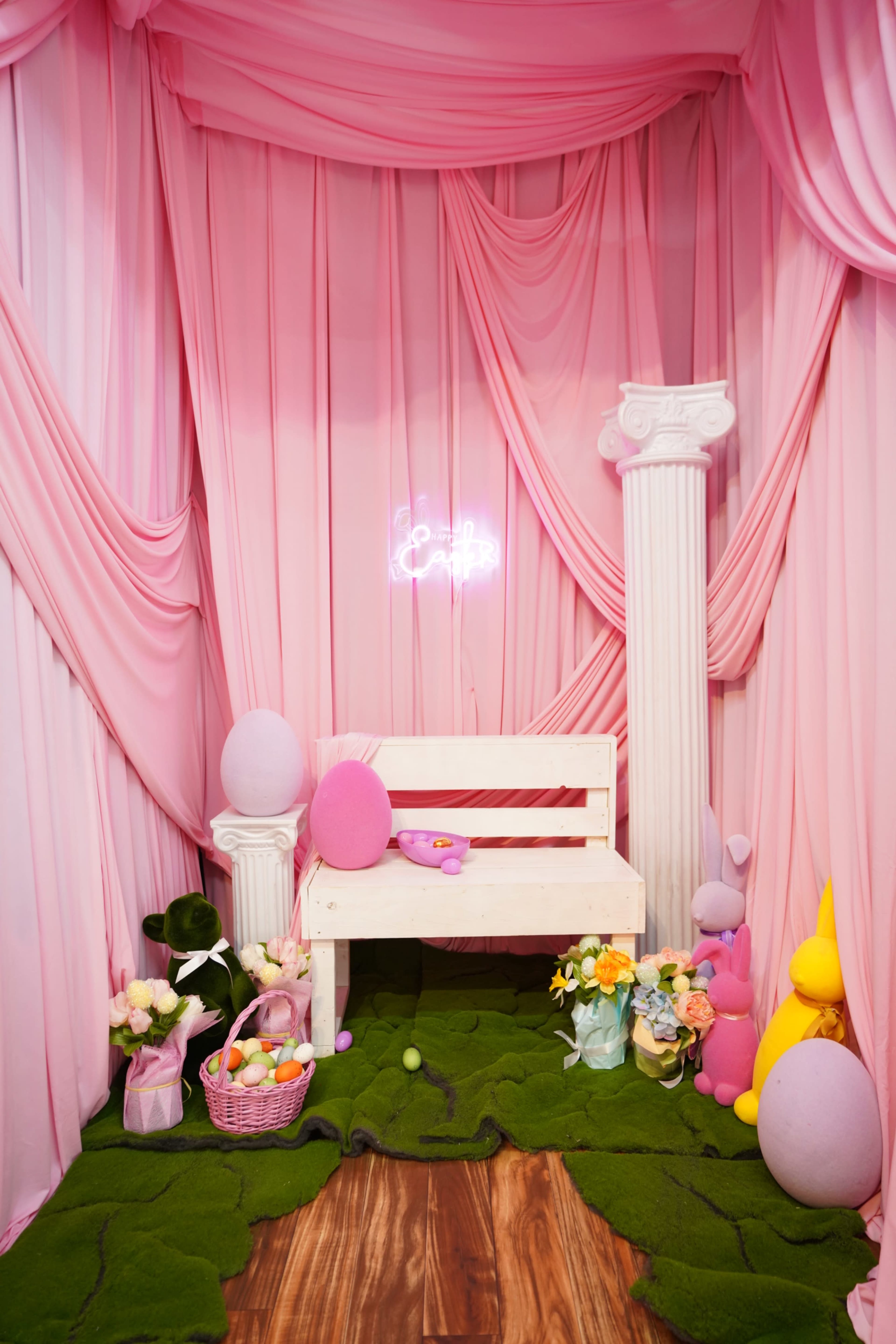 The scene features a decorated area with pink draped fabric, a white wooden bench, and Easter-themed decorations including colored eggs and flowers.