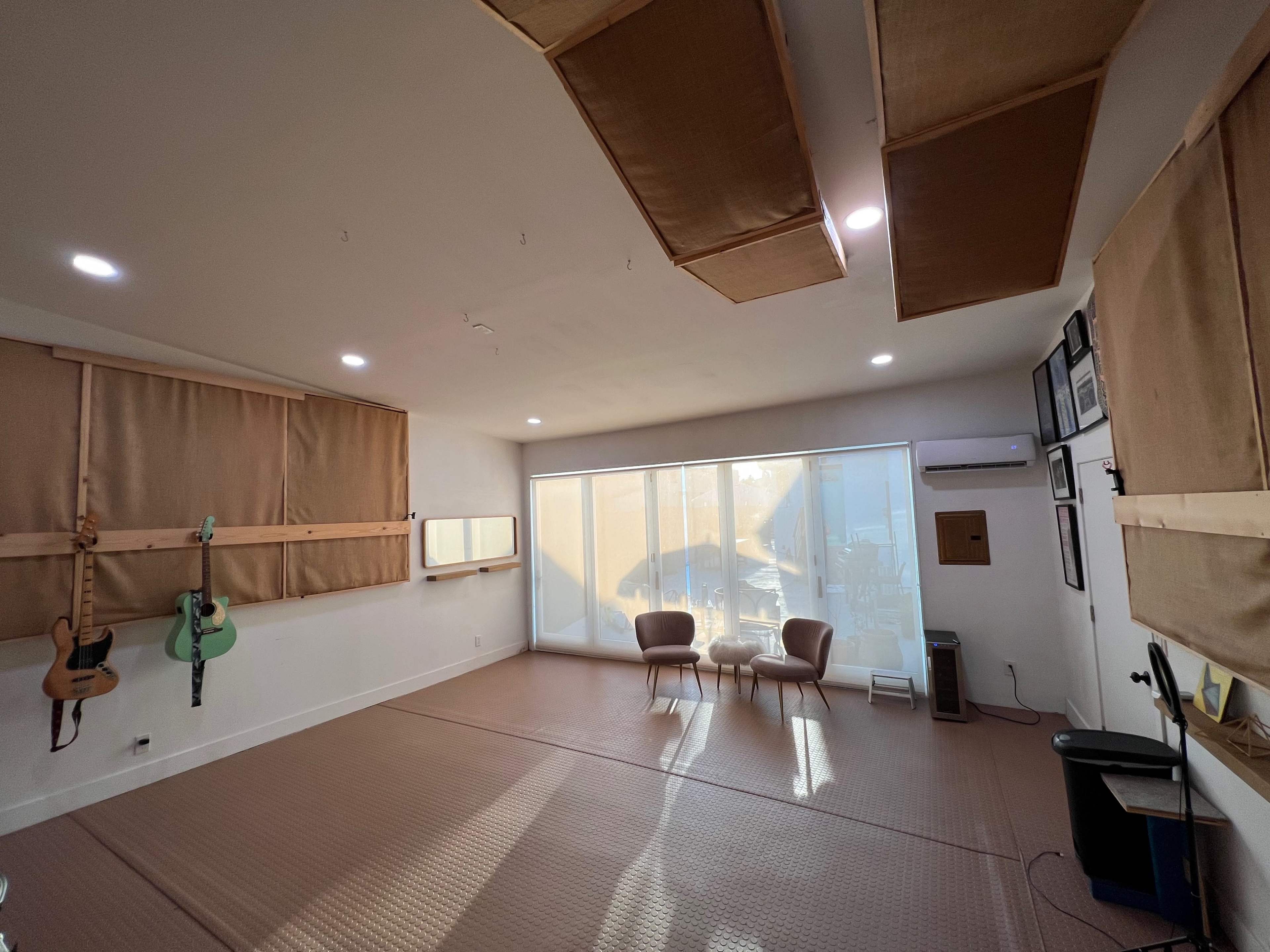The image shows a spacious music studio with two chairs, large windows, and guitars mounted on the walls.