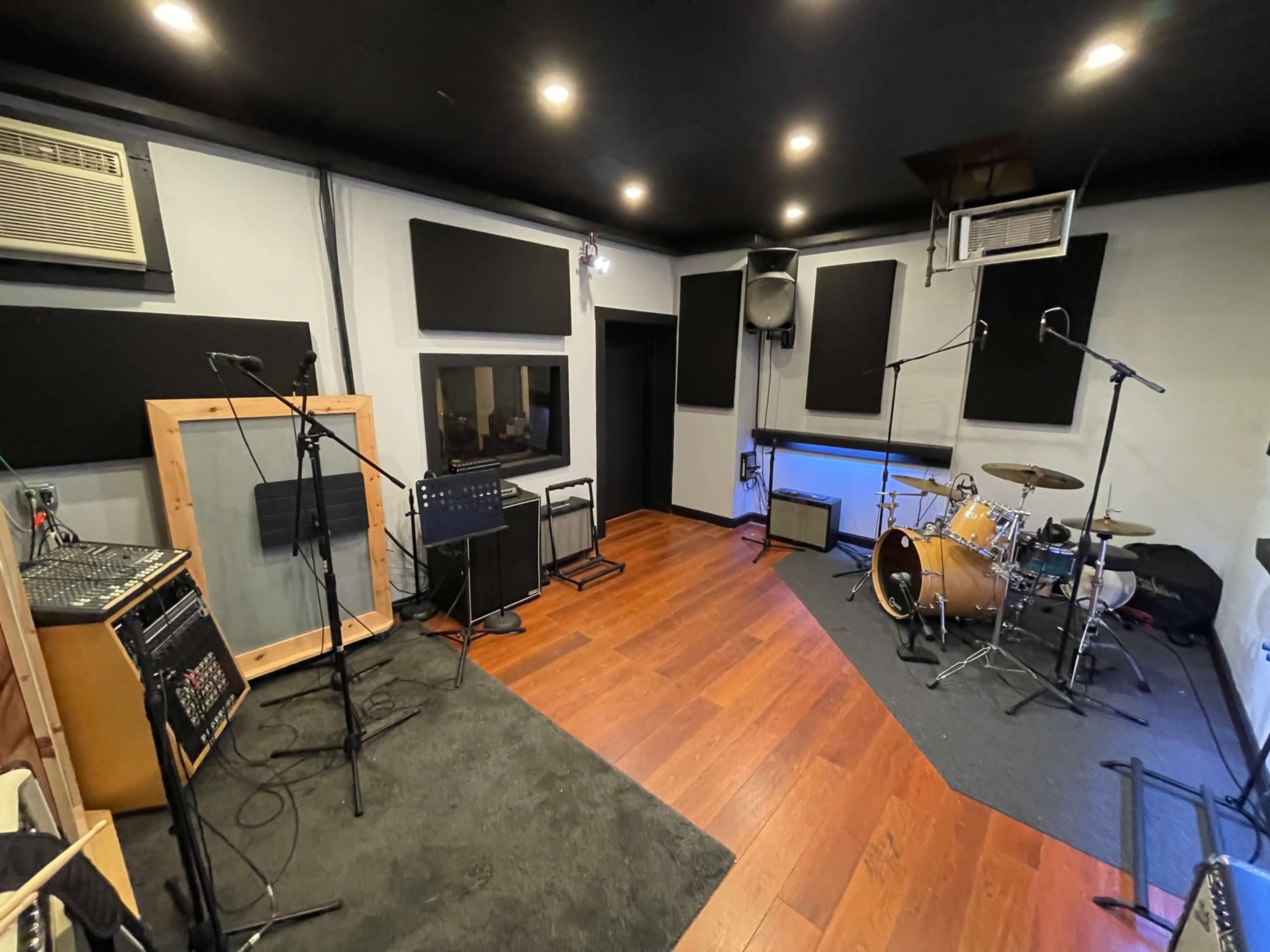A music recording studio with soundproof panels, a drum set, microphones, and a sound mixer.