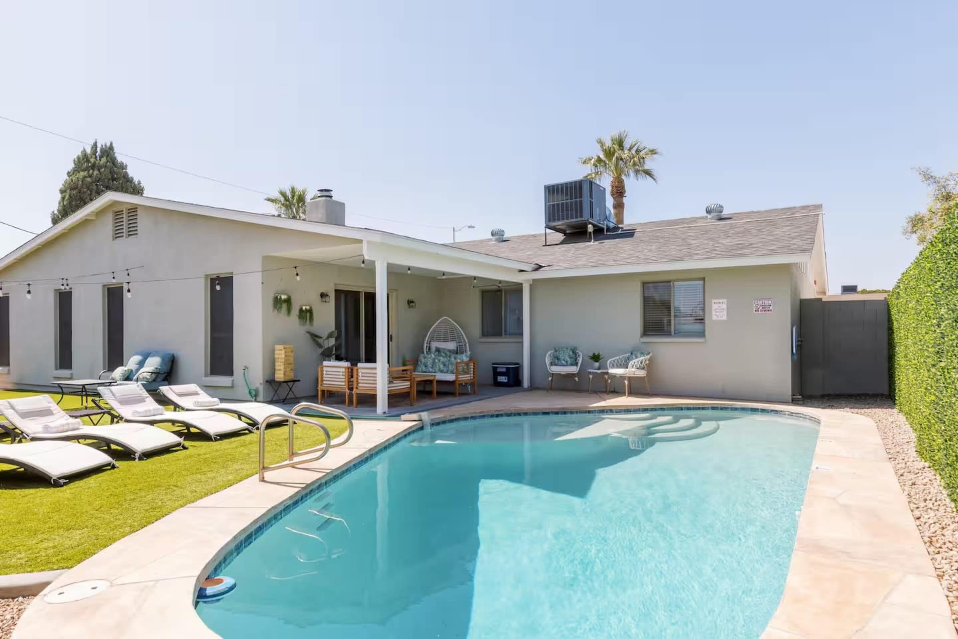 The image shows a backyard with a swimming pool, lounge chairs, and a small house with a covered patio and palm trees.