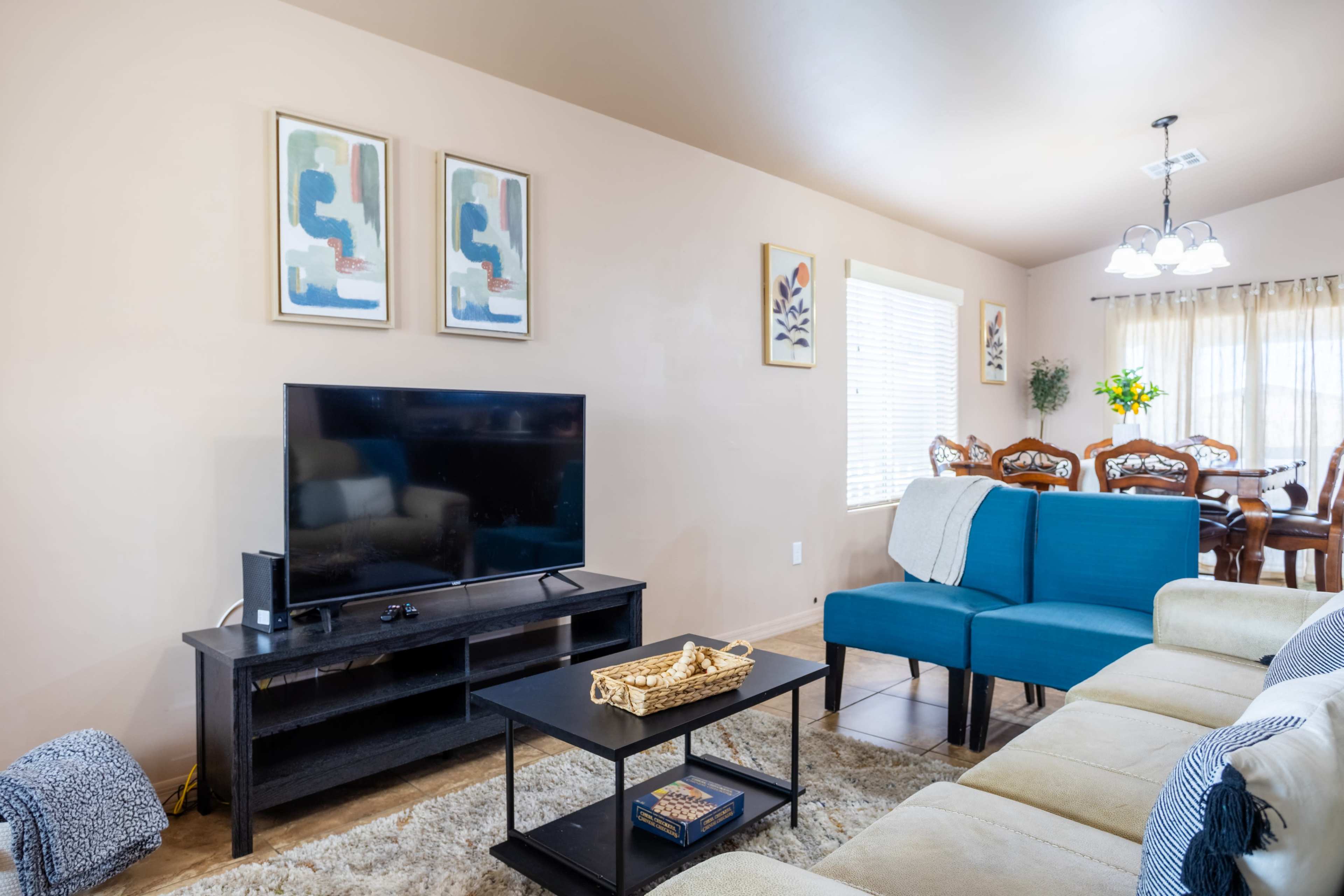 A living room with a blue sectional sofa, a black coffee table, a television stand, and dining area in the background.