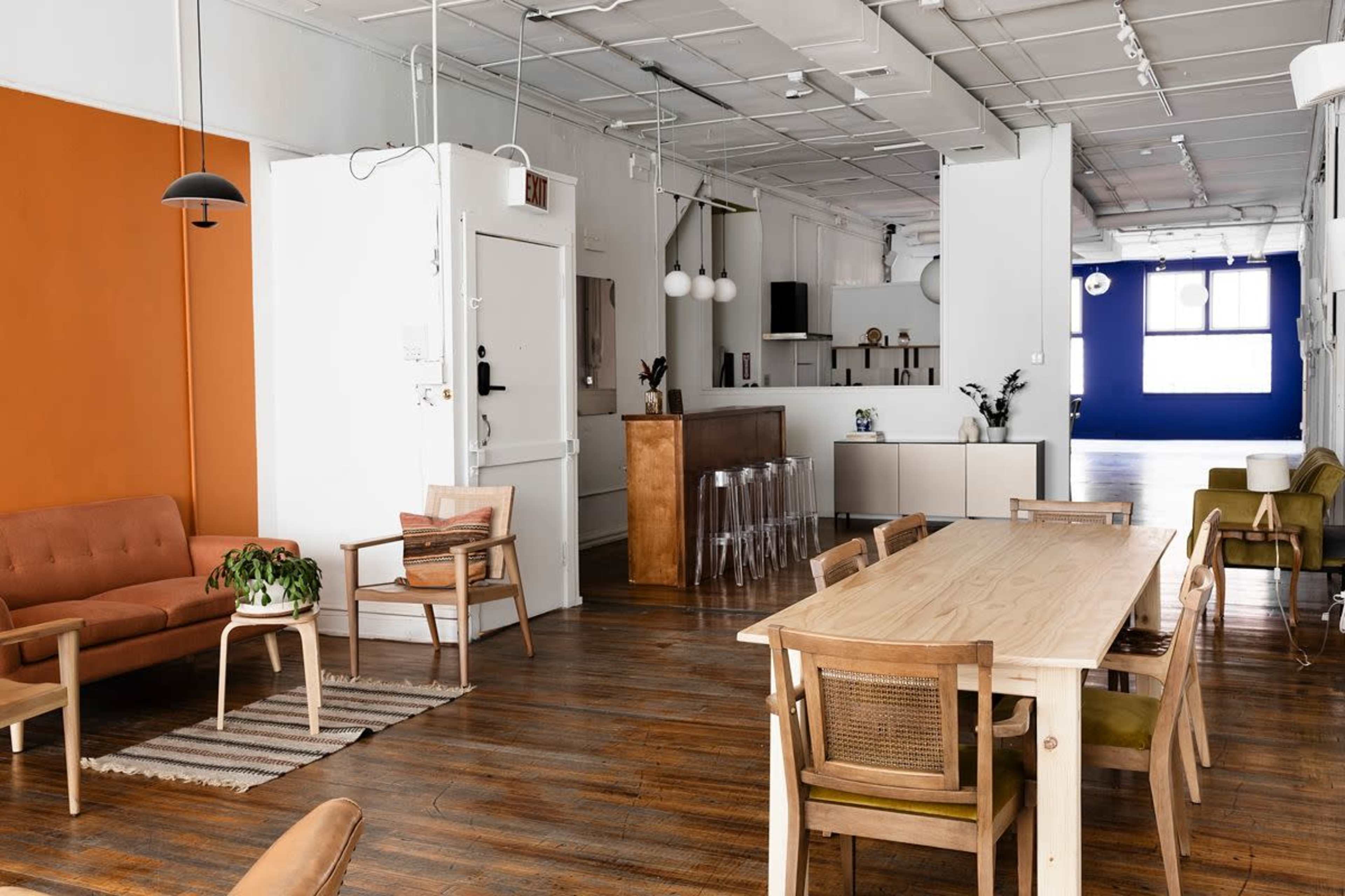 The image shows a modern, open-plan interior featuring a mix of seating areas, a dining table, and vibrant wall colors.