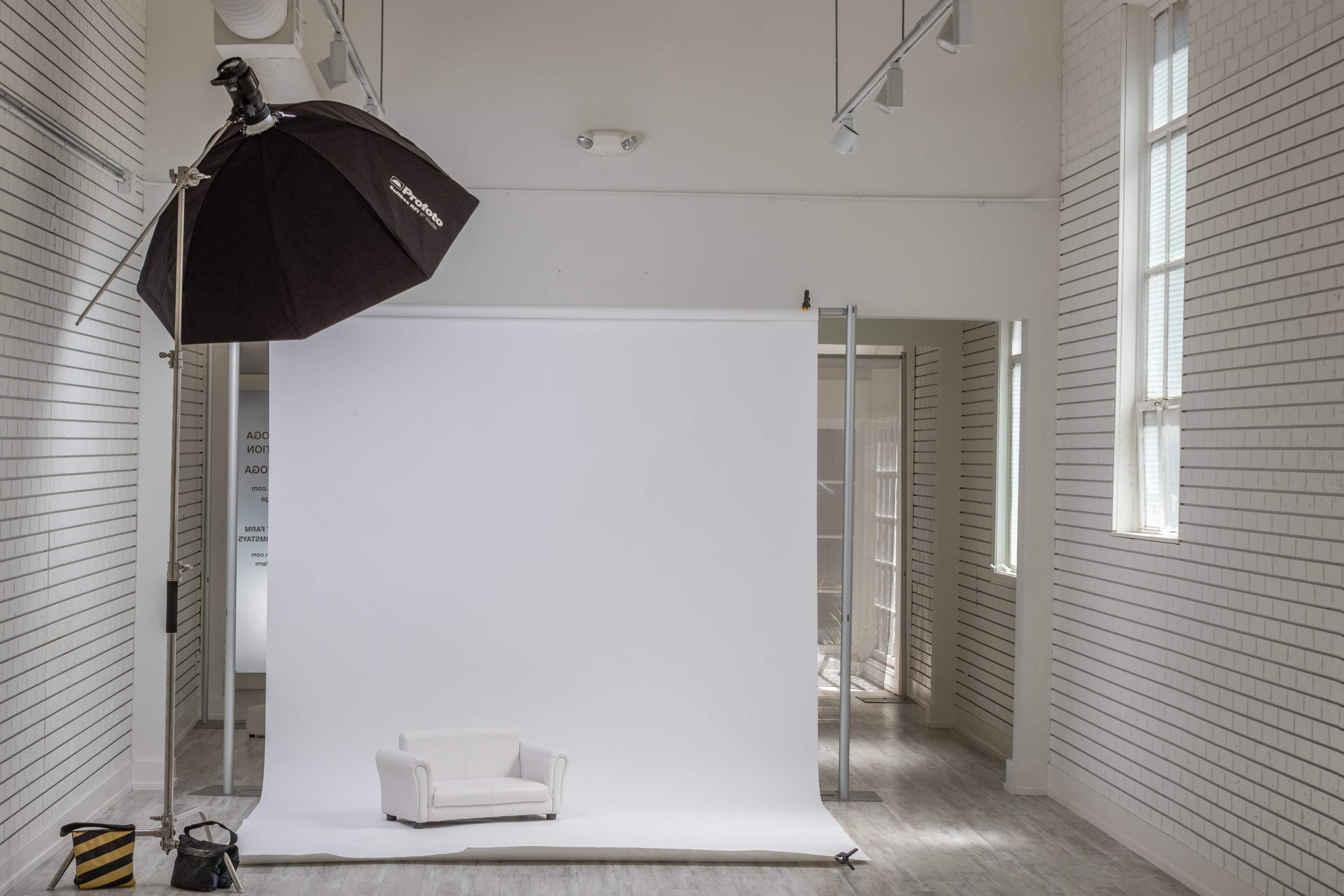 A minimalist photography studio with a white backdrop, a small white couch, and a large softbox light setup.