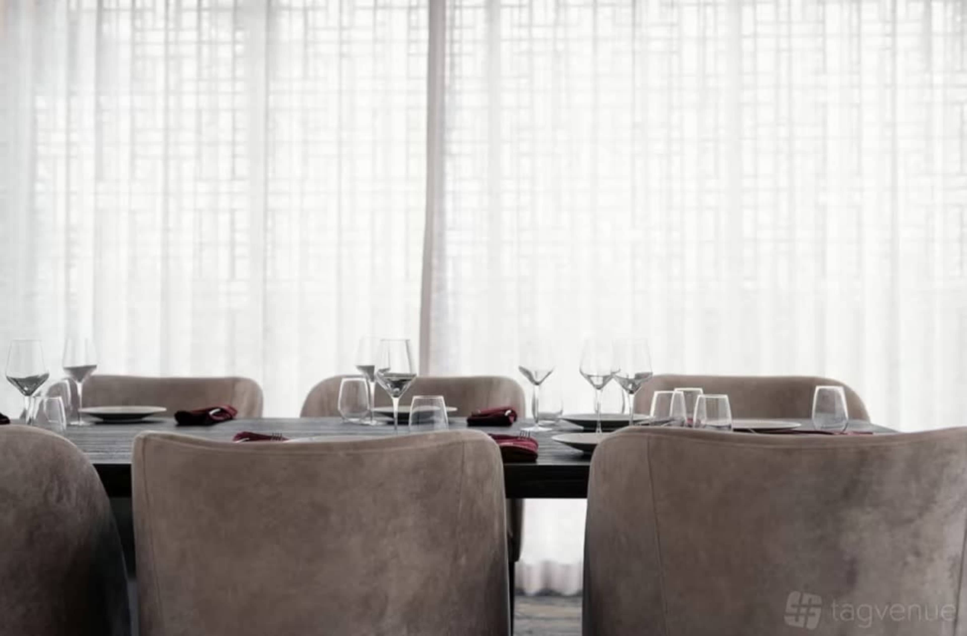 A dining area set with glassware and folded napkins around a dark wooden table.