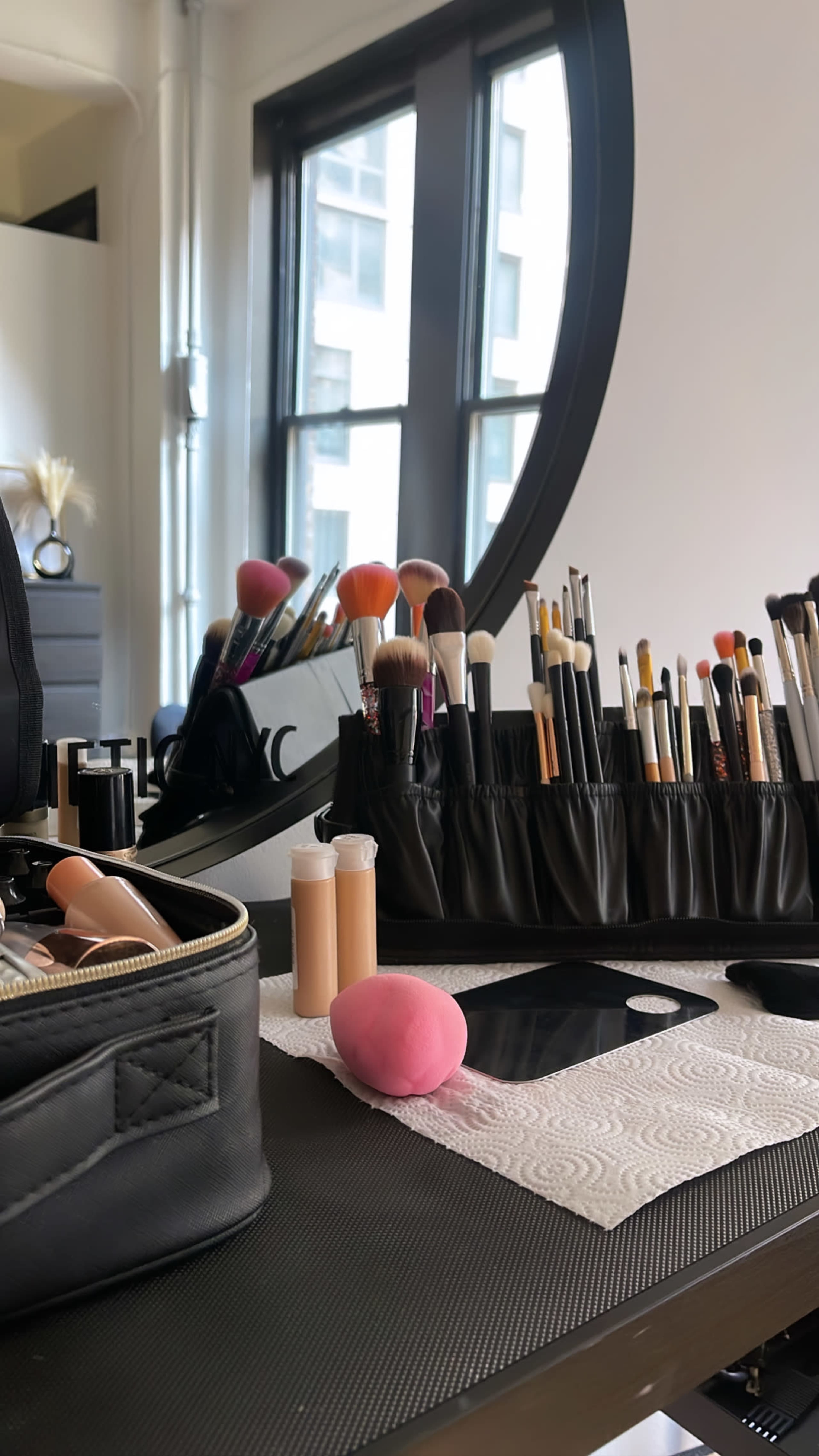 A makeup station displays various brushes neatly arranged in a holder, along with beauty sponges and foundation tubes on a clean surface.