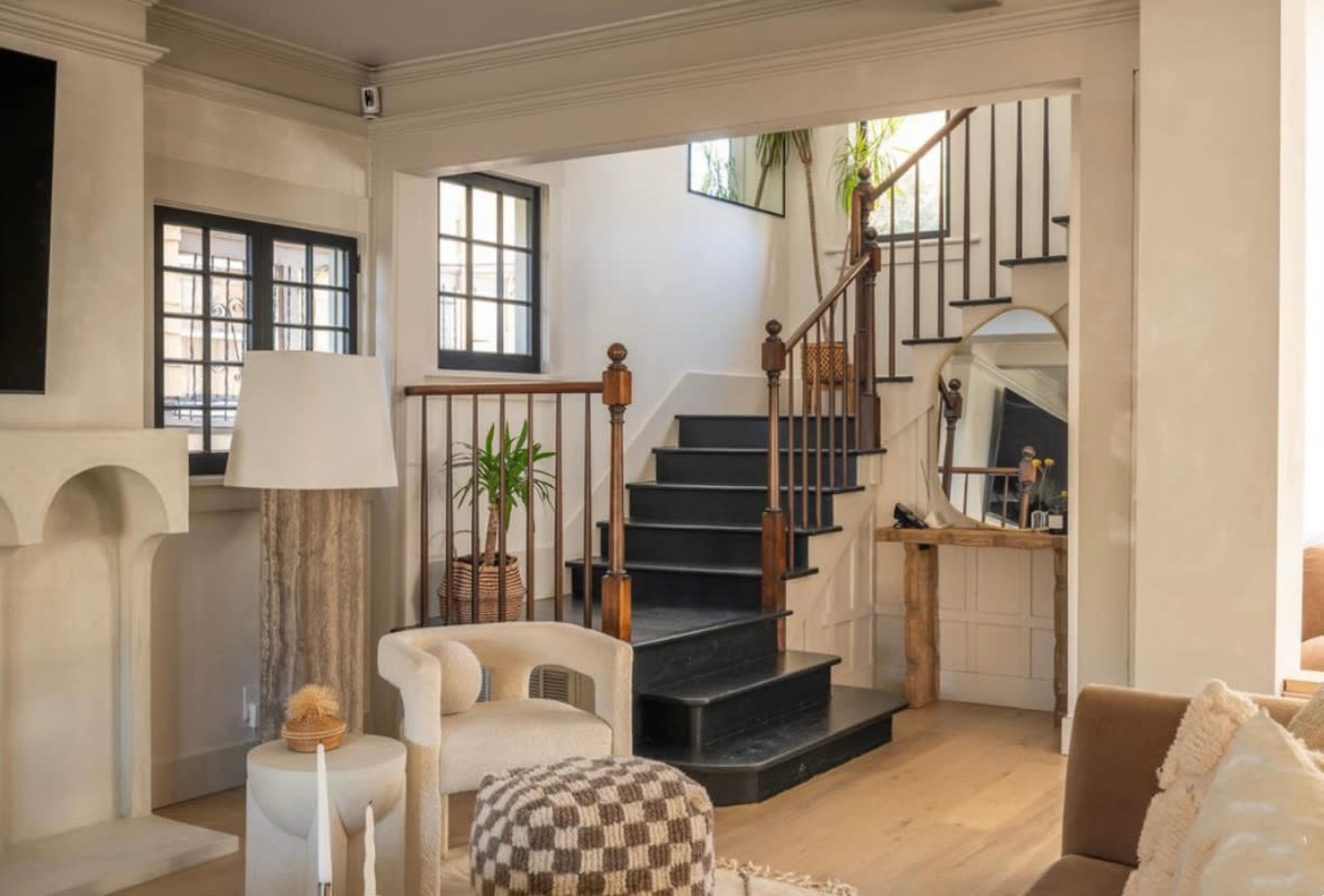 The image shows a modern living room with a staircase leading to an upper level and a combination of light-colored walls and wooden accents.