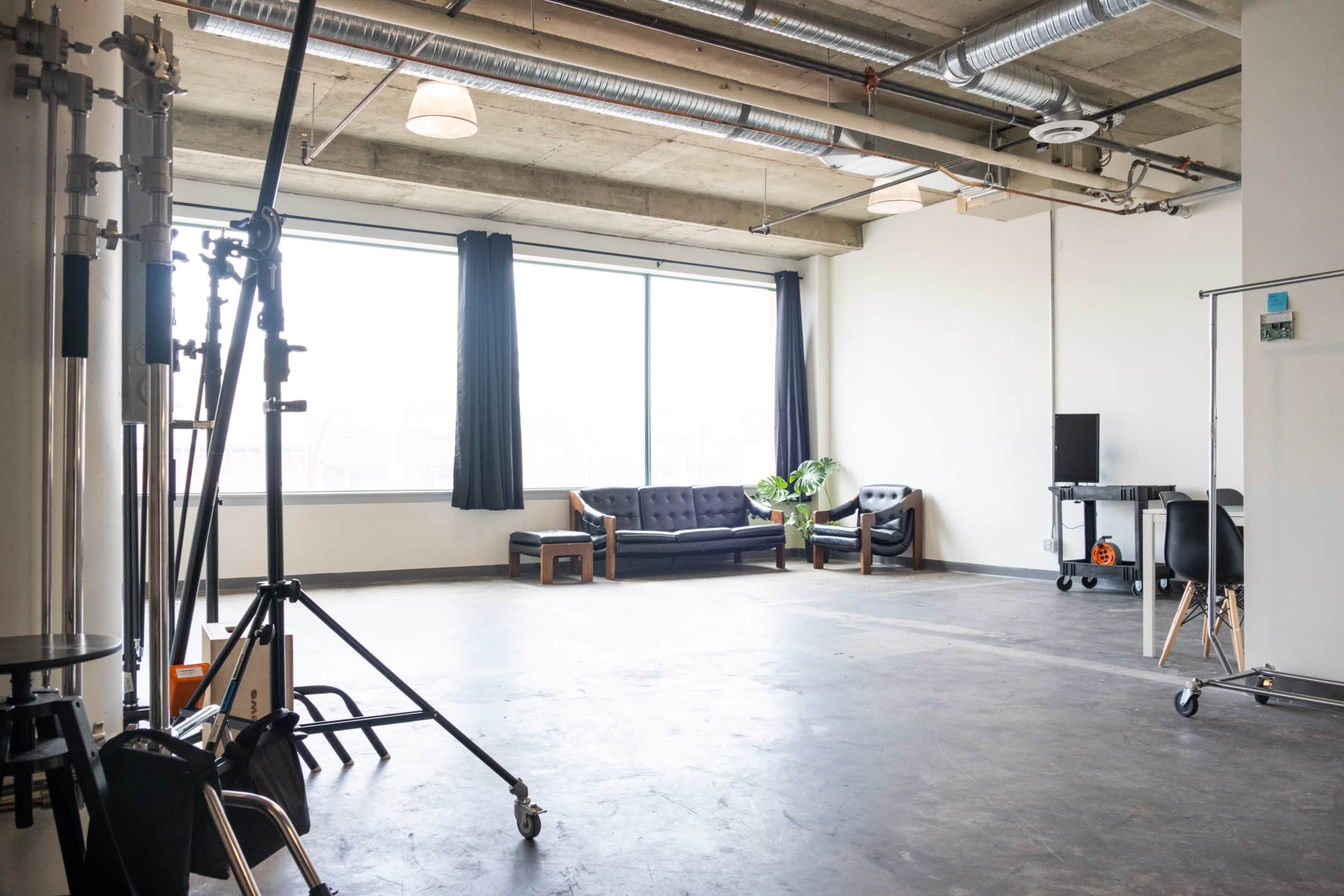 A spacious room with large windows, featuring a sofa, armchairs, and studio equipment.