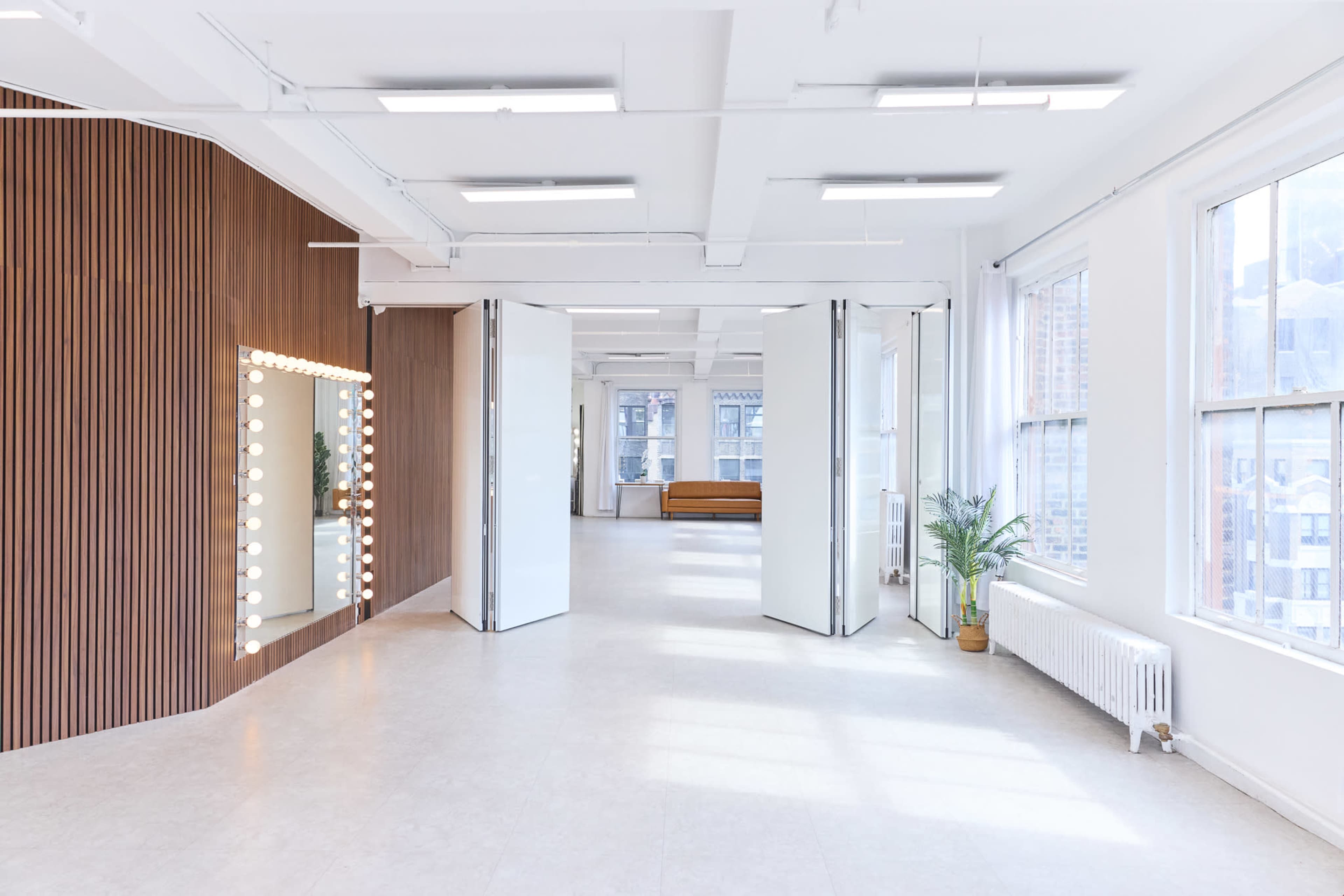 The image shows a spacious, well-lit interior with wooden and mirrored wall features, and large windows providing ample natural light.