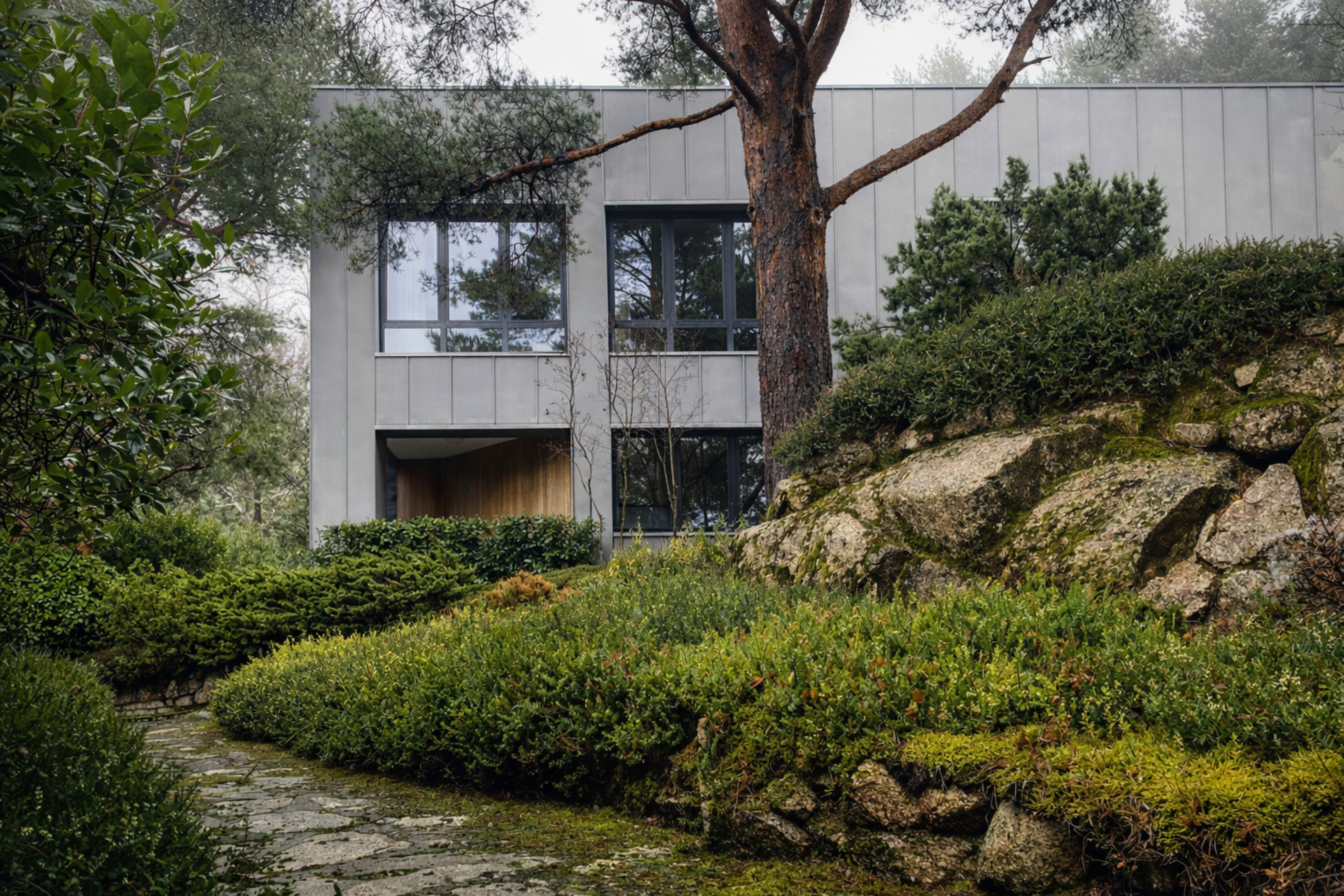A modern house with large windows is situated among lush greenery and rocky landscaping.