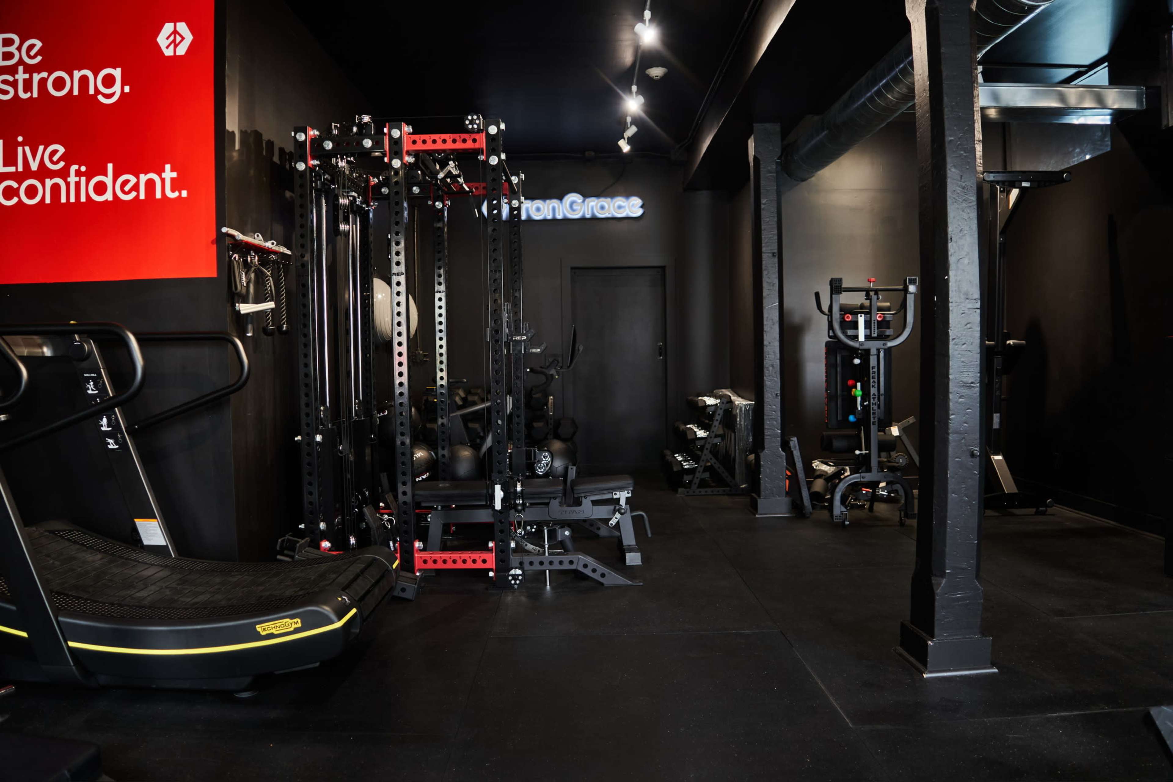 The image shows a modern gym interior featuring various exercise equipment, including a treadmill, weight machines, and a cable machine, set against a sleek black background.