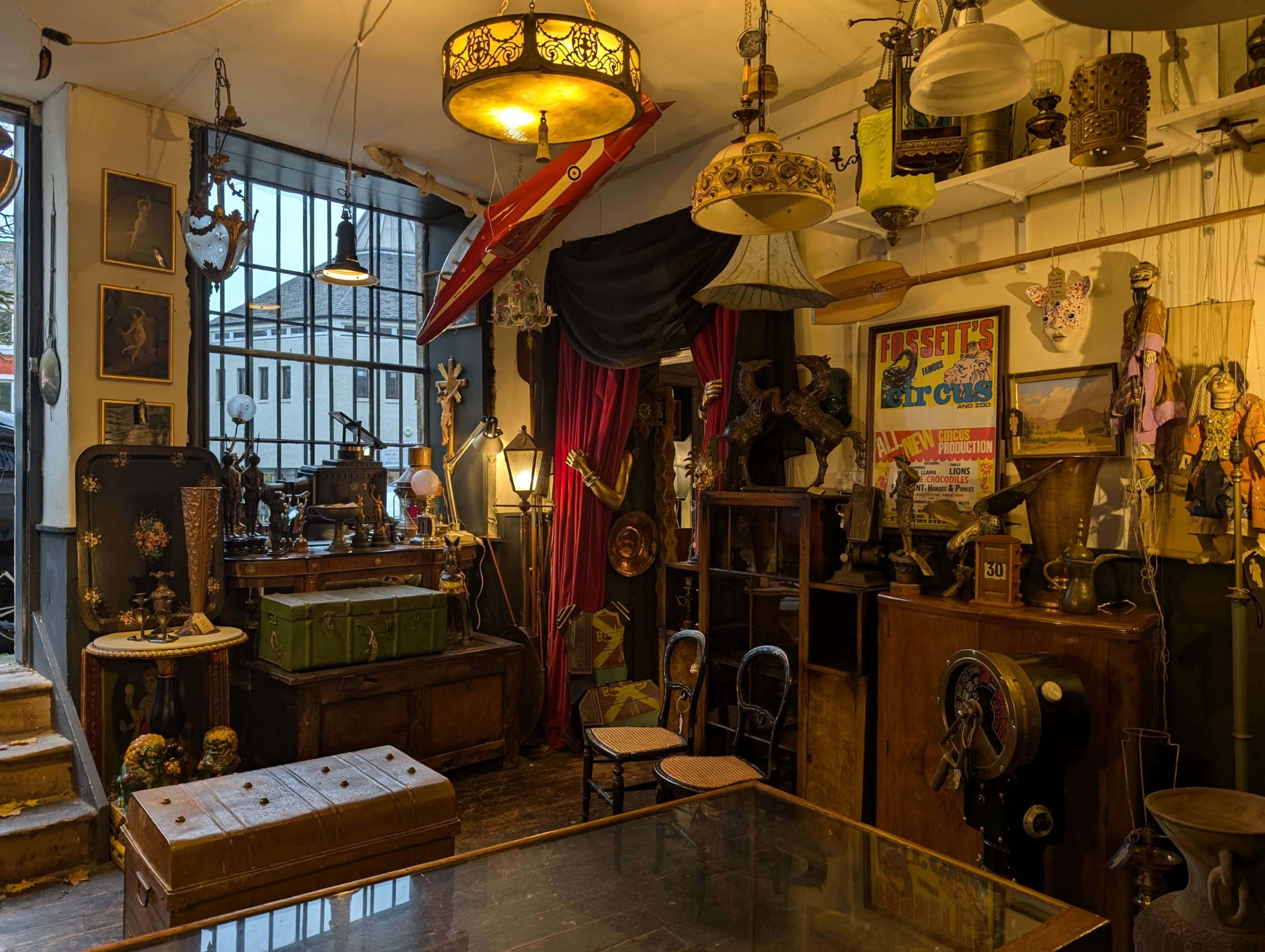 The scene features a vintage shop filled with an assortment of antique items, including lamps, furniture, and decorative objects, arranged around a central table.