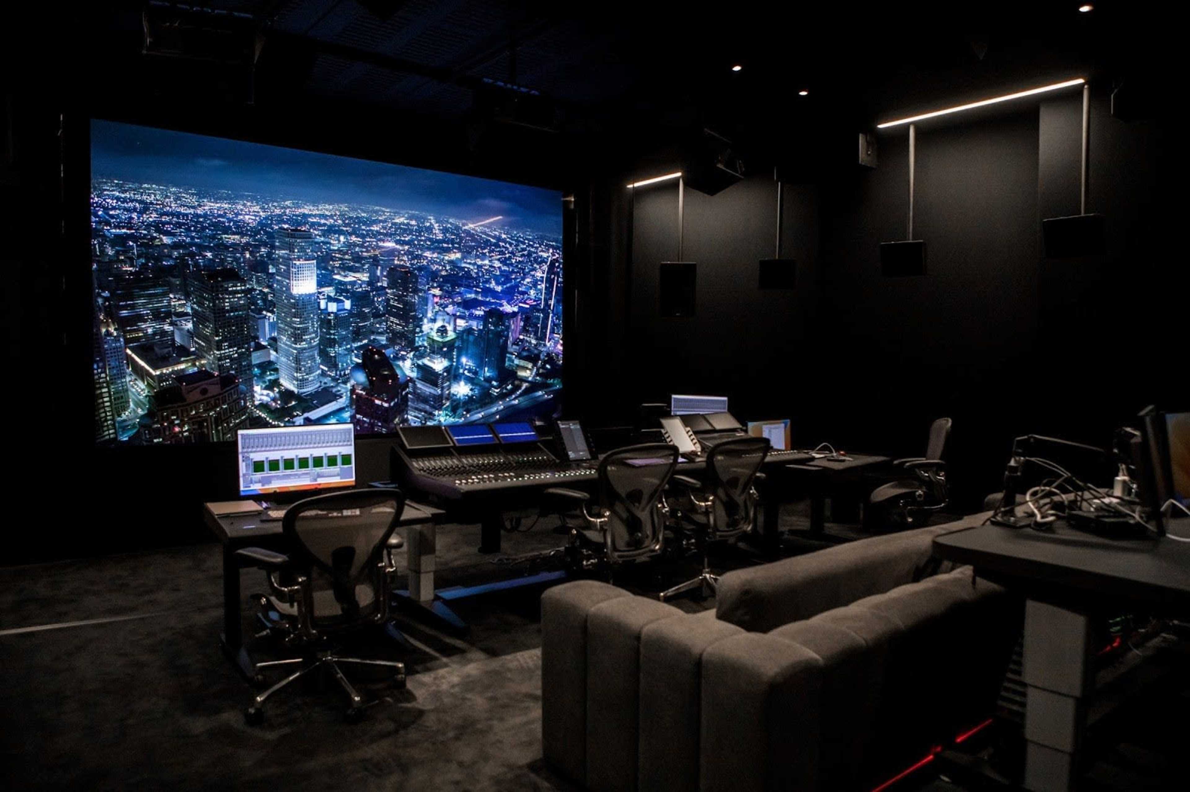 A modern audio-visual studio features multiple workstations and a large screen displaying a city skyline at night.