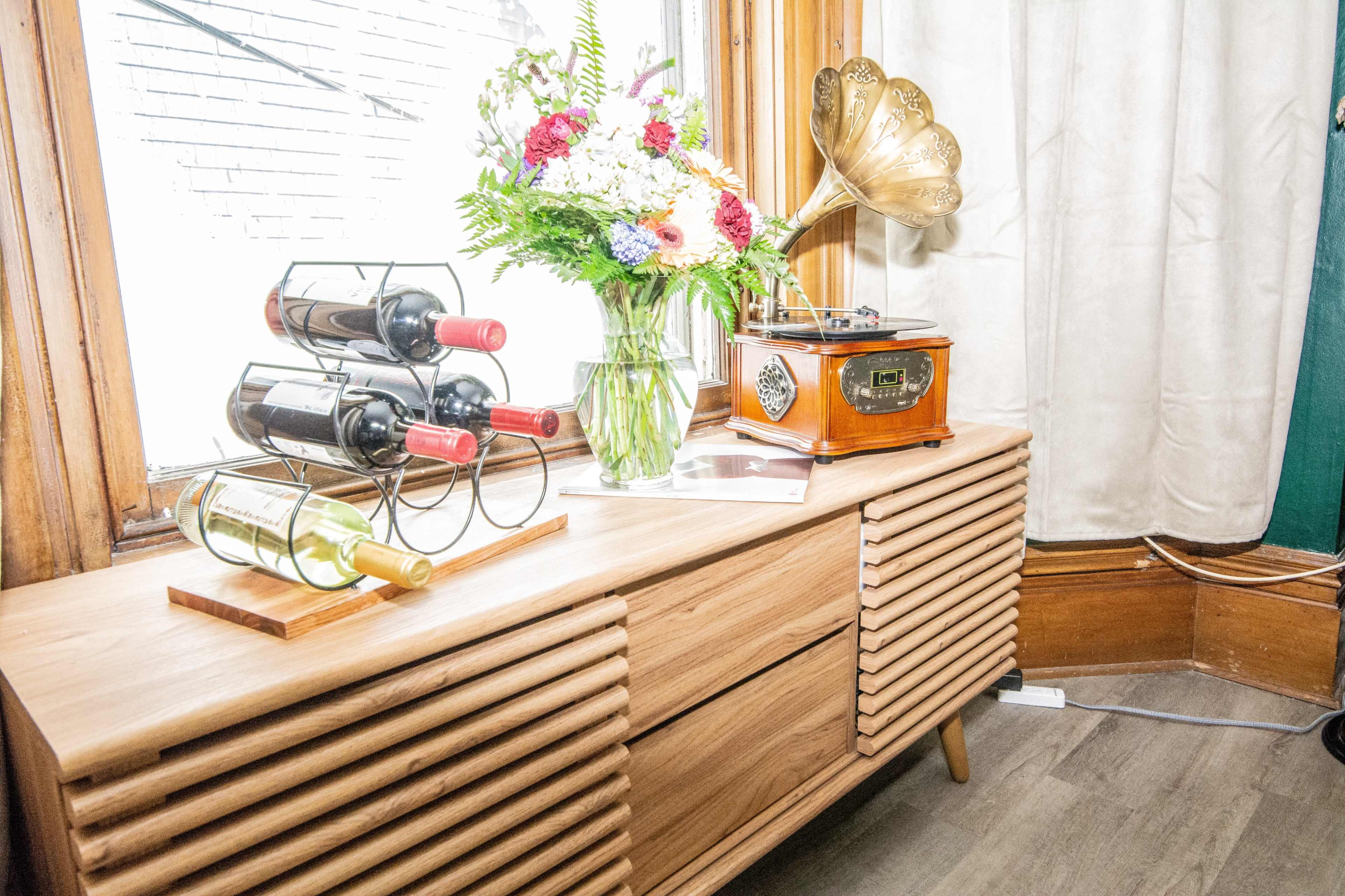A wooden console table displays a vintage record player, a vase of flowers, and a wine rack holding several bottles.