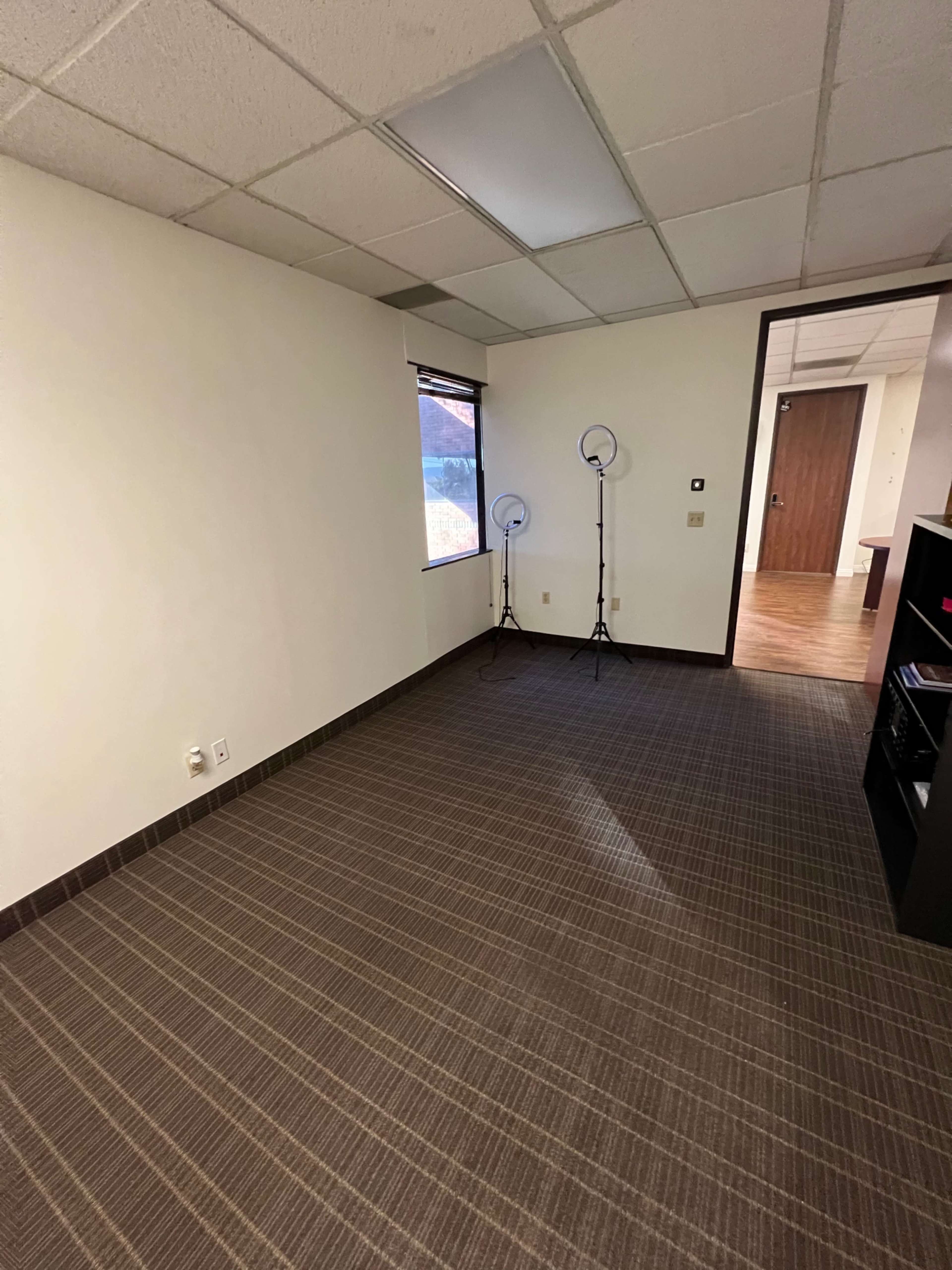 A vacant office space with a window and two light stands in one corner, featuring a tiled floor and plain walls.