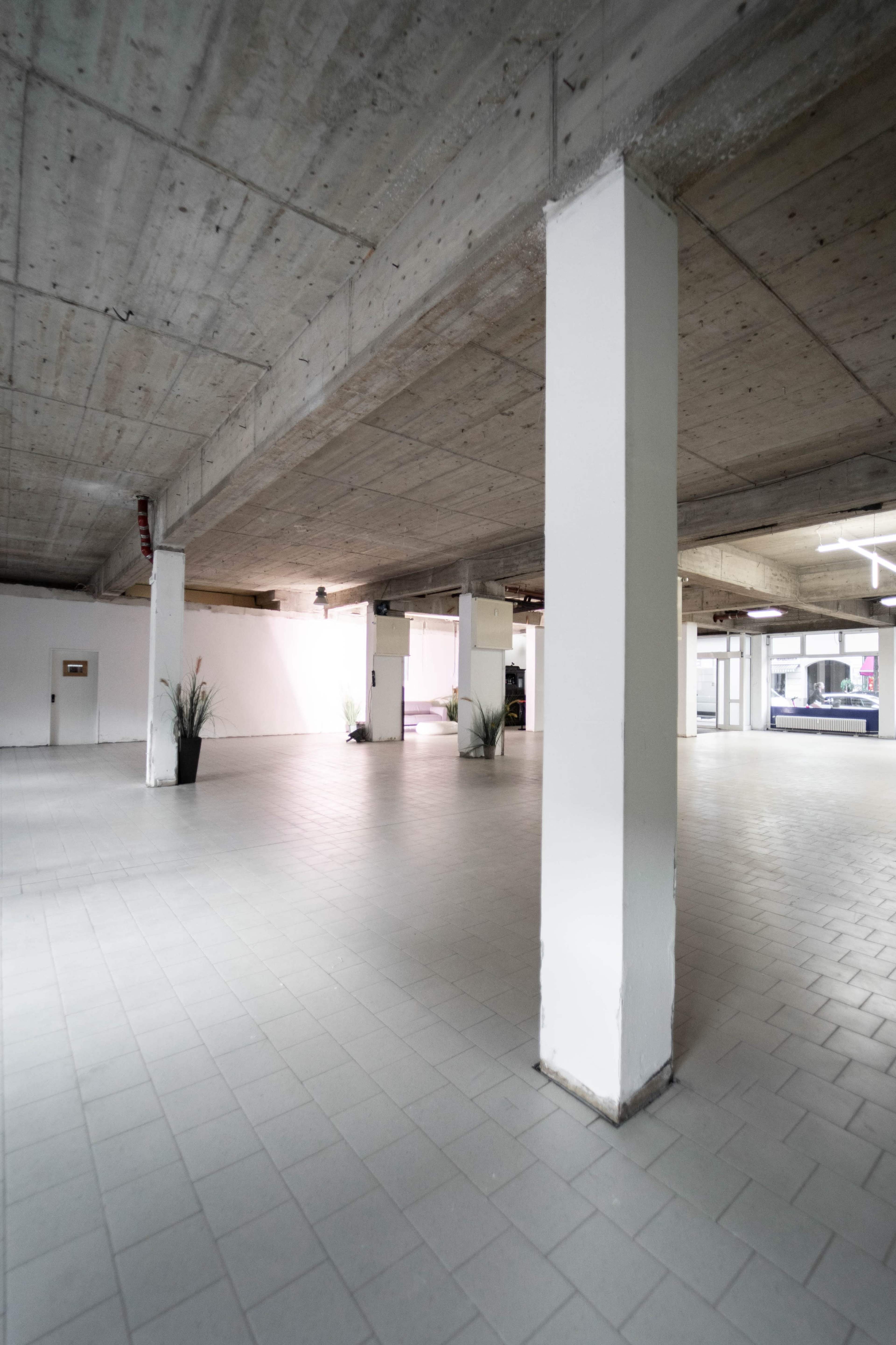 The image shows an empty underground parking garage with concrete pillars and smooth tiled flooring.
