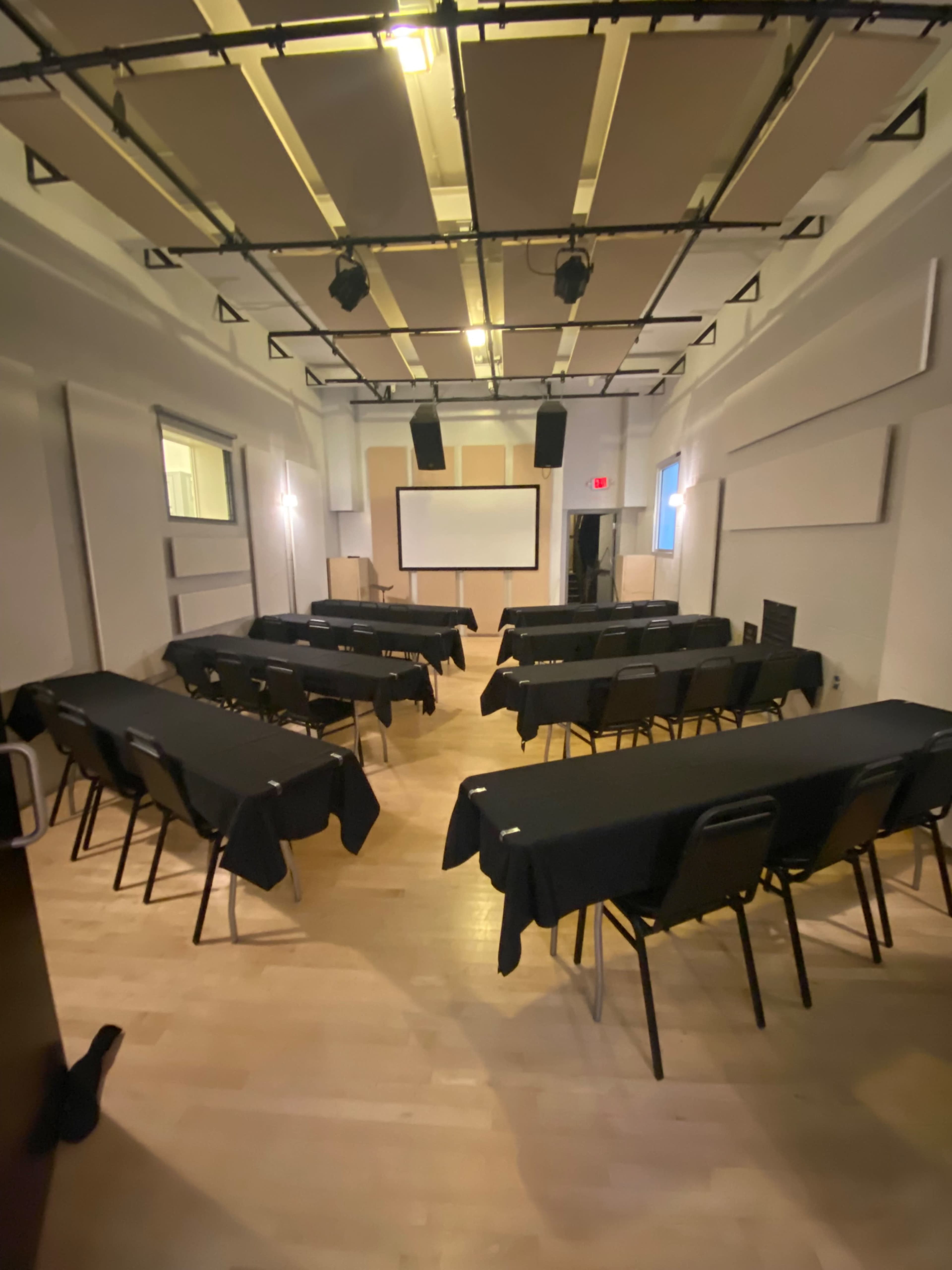A conference room is set up with rows of tables covered in black cloth and chairs arranged for a presentation.