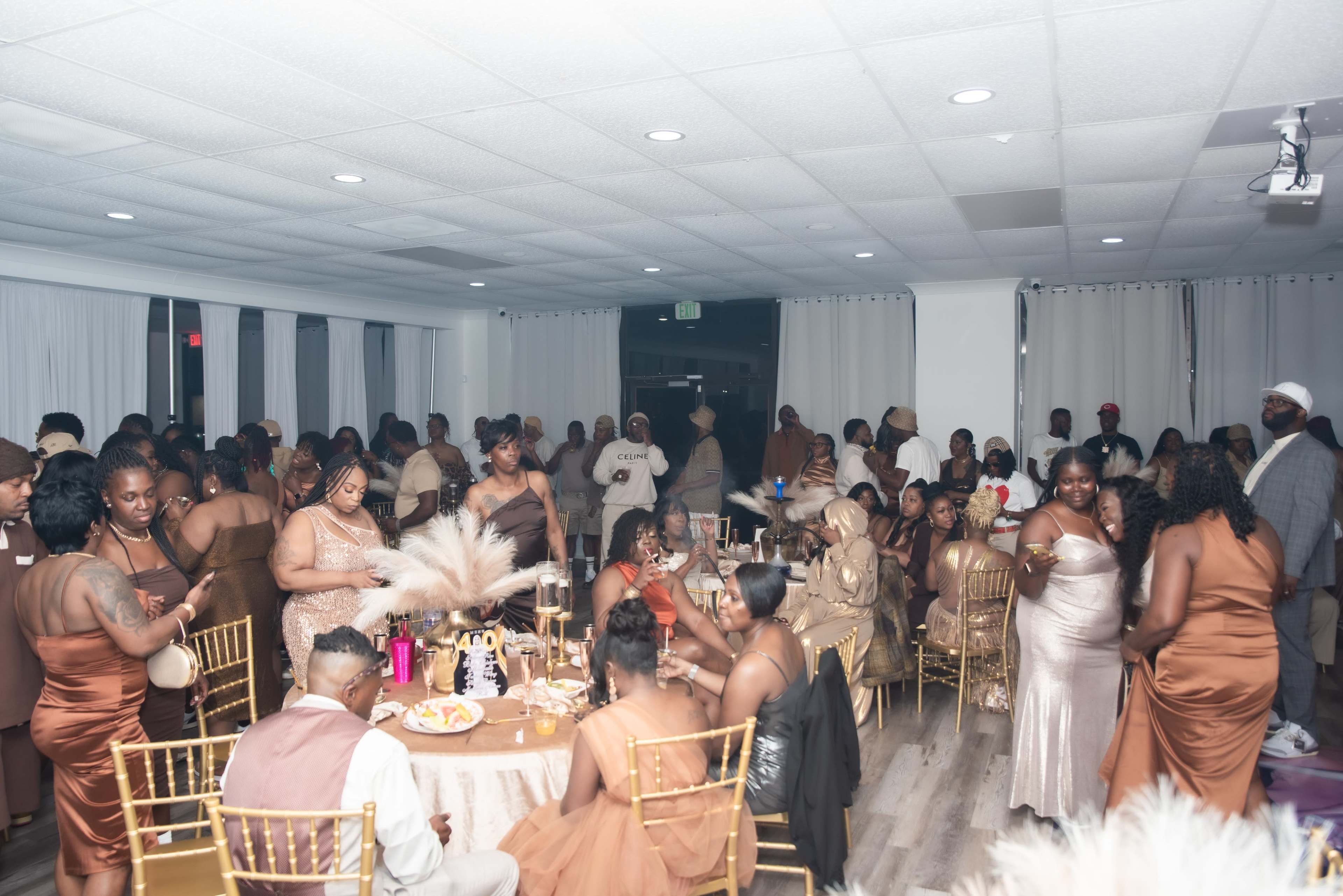 A large group of people dressed in formal attire gather at elegantly decorated tables in a well-lit event space.