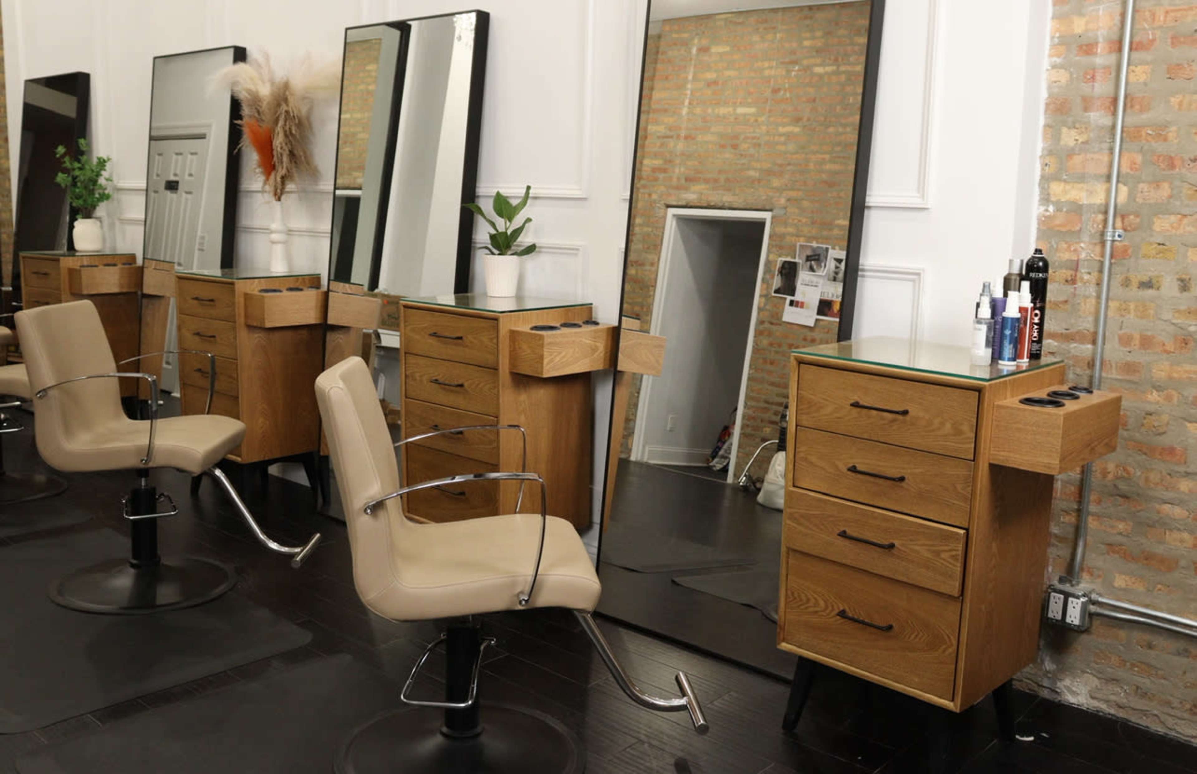 The image shows a modern hair salon featuring several wooden styling stations with mirrors, comfortable chairs, and storage drawers.