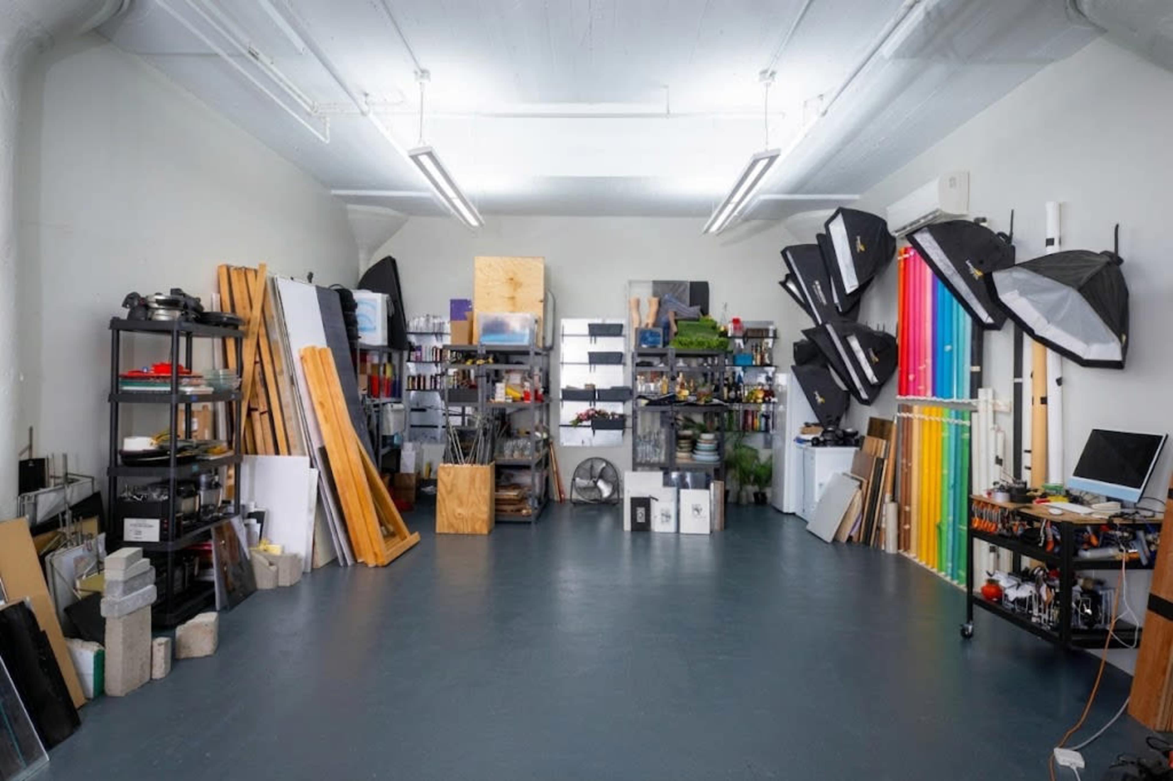 The image shows a spacious studio filled with various photography equipment, props, and storage shelves organized along the walls.