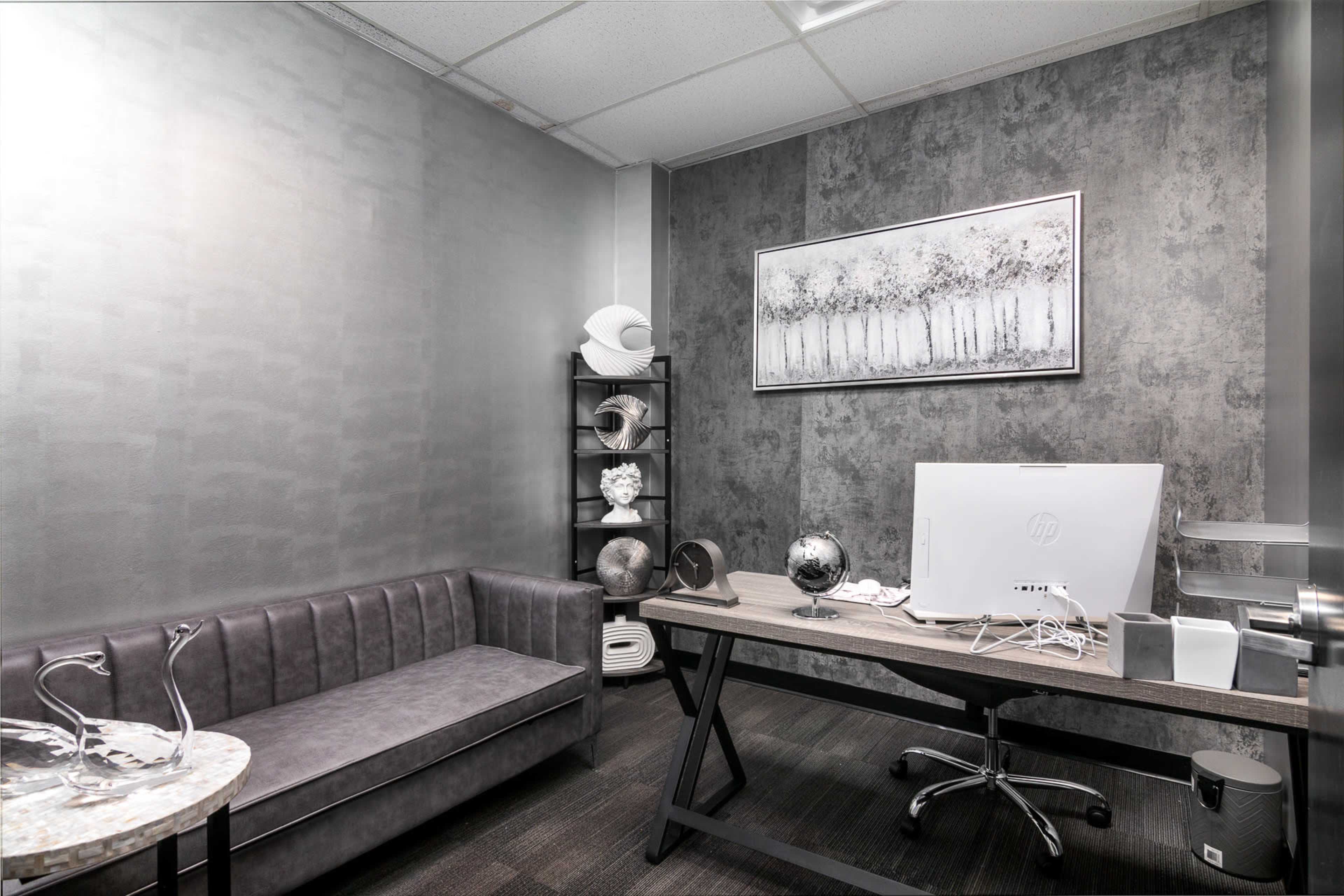 A modern office space with a gray color scheme, featuring a sofa, a desk with a computer, and decorative items on a shelf.
