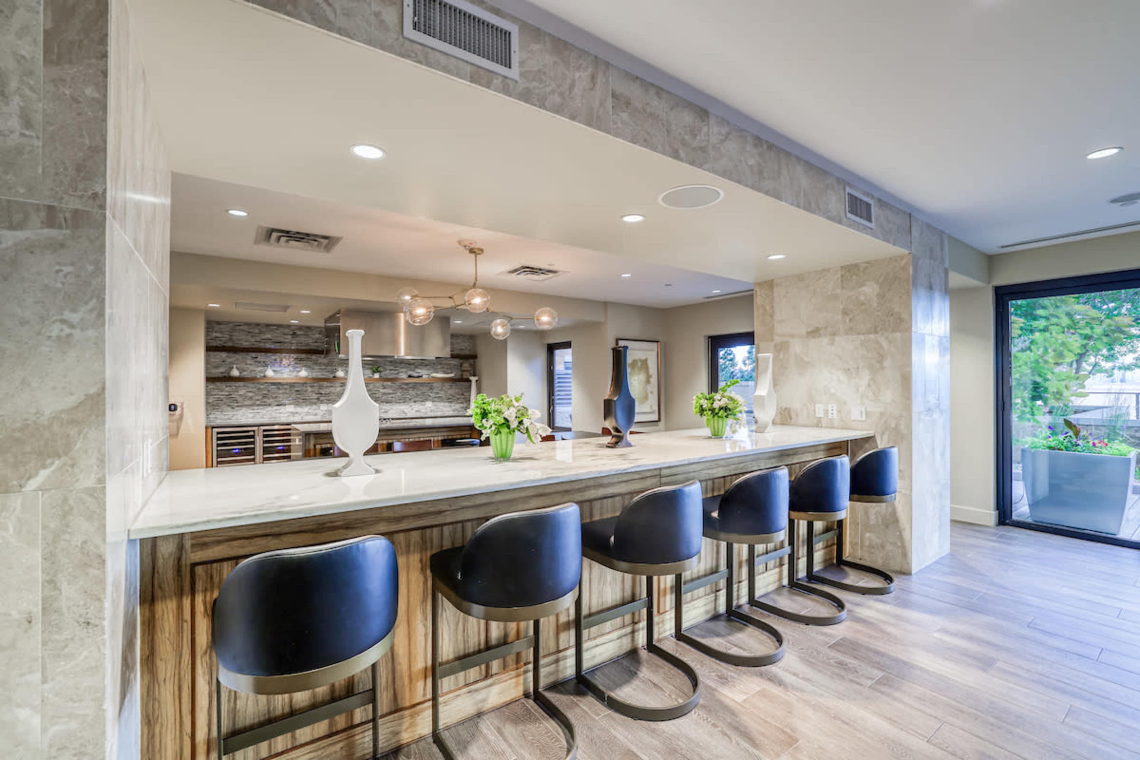 A modern kitchen with a large island bar featuring black stools, surrounded by light-colored cabinetry and a spacious layout.