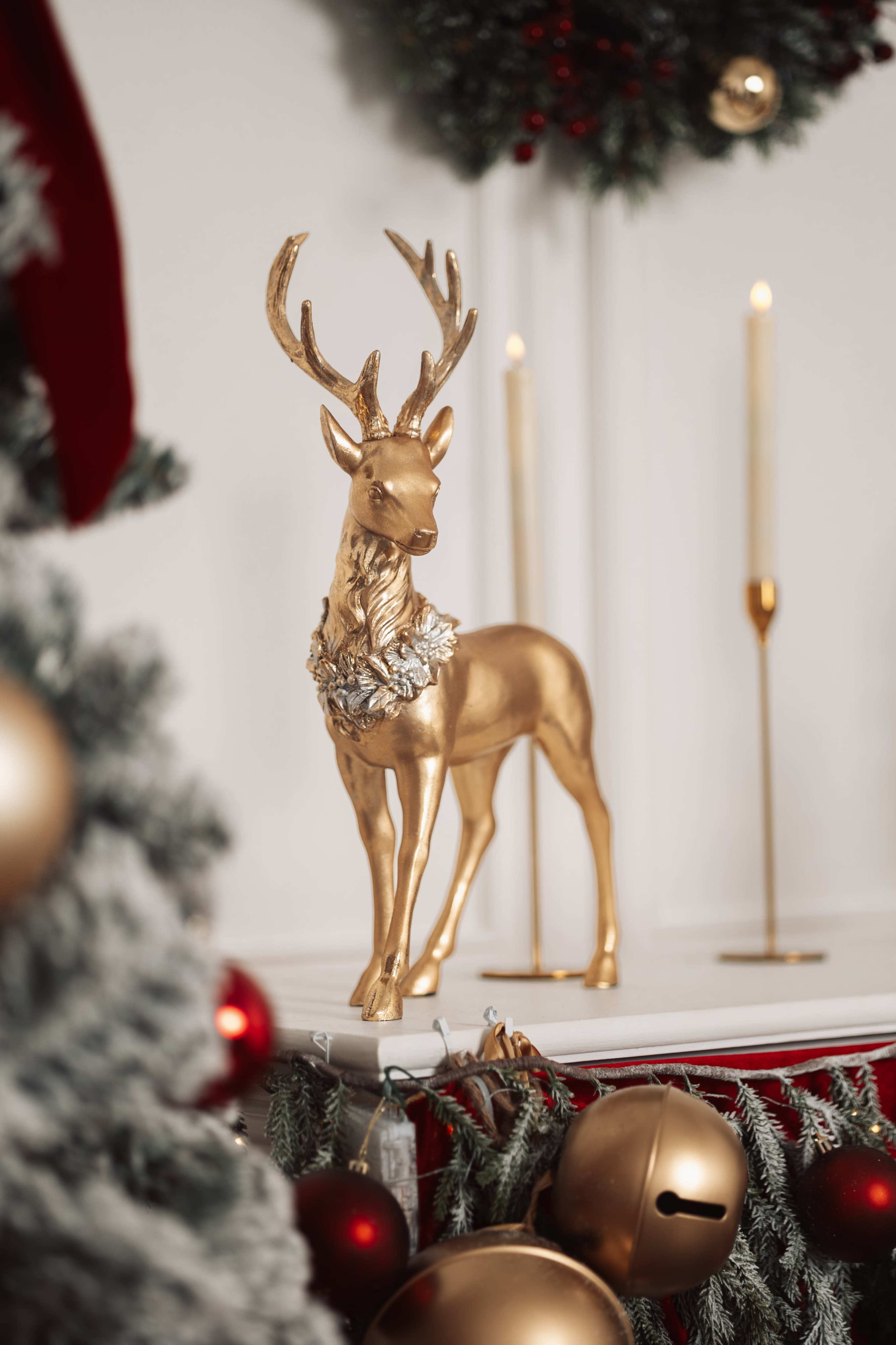 A gold-painted reindeer statue adorned with a wreath stands on a mantle decorated with festive ornaments and candles.