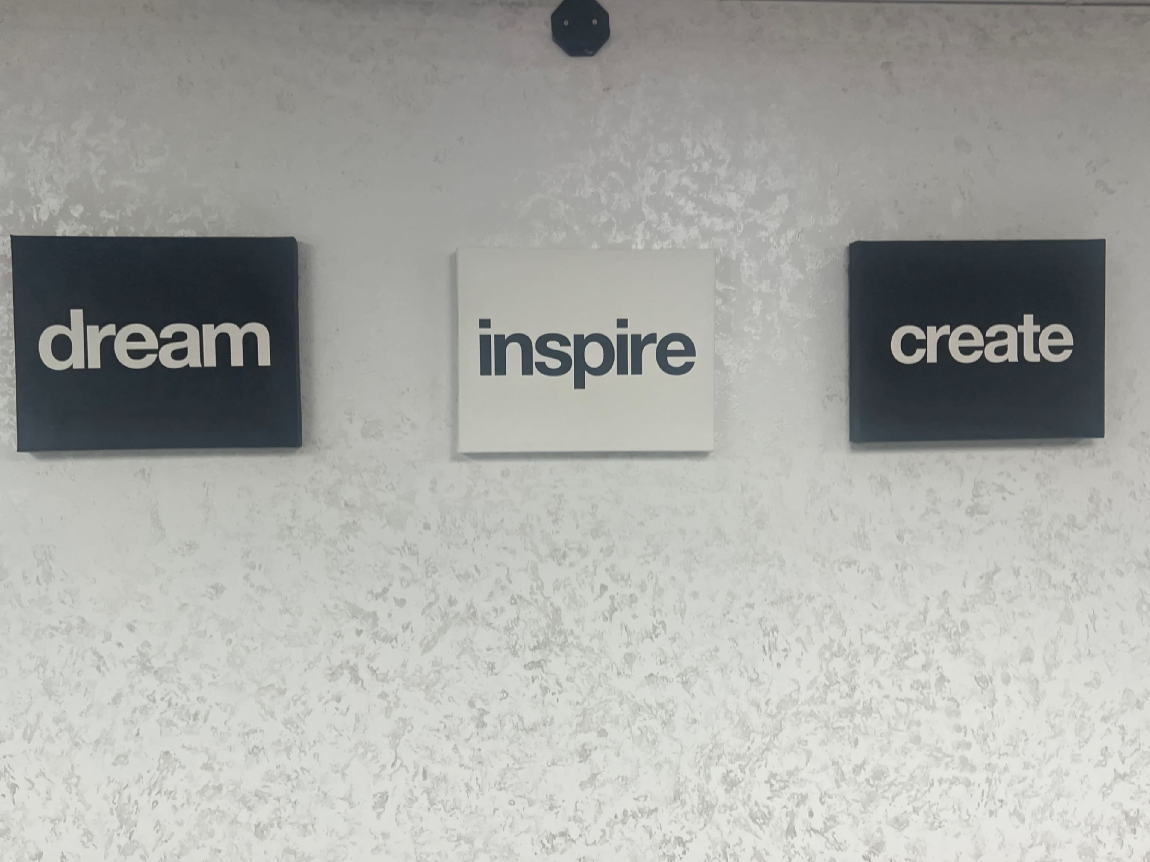 Three canvas prints featuring the words "dream," "inspire," and "create" are displayed on a textured white wall.