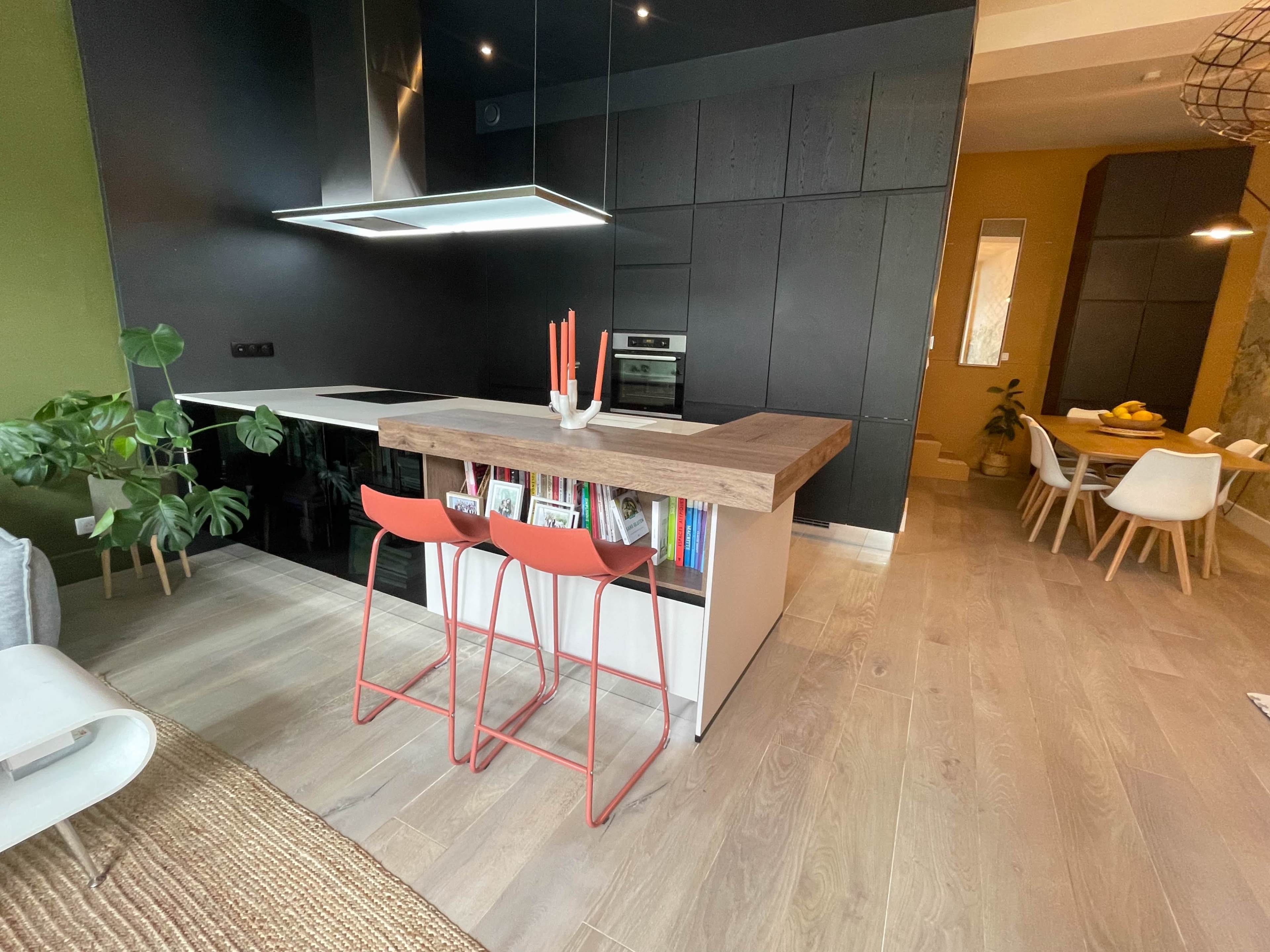 The image shows a modern kitchen with a wooden island, black cabinetry, and a dining area in a well-lit space.