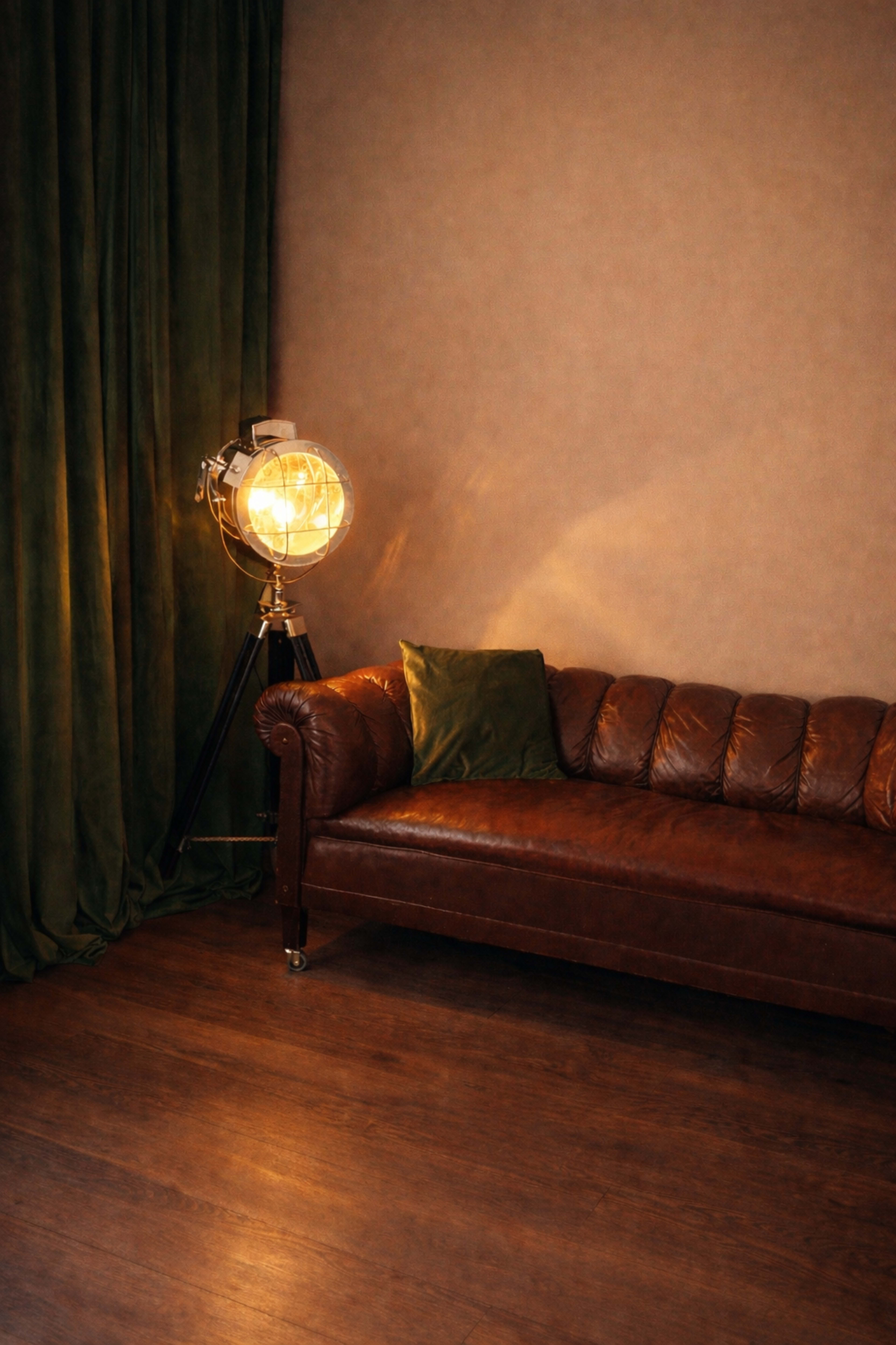 A brown leather sofa is positioned against a wall, next to a large green curtain and a spotlight on a tripod.