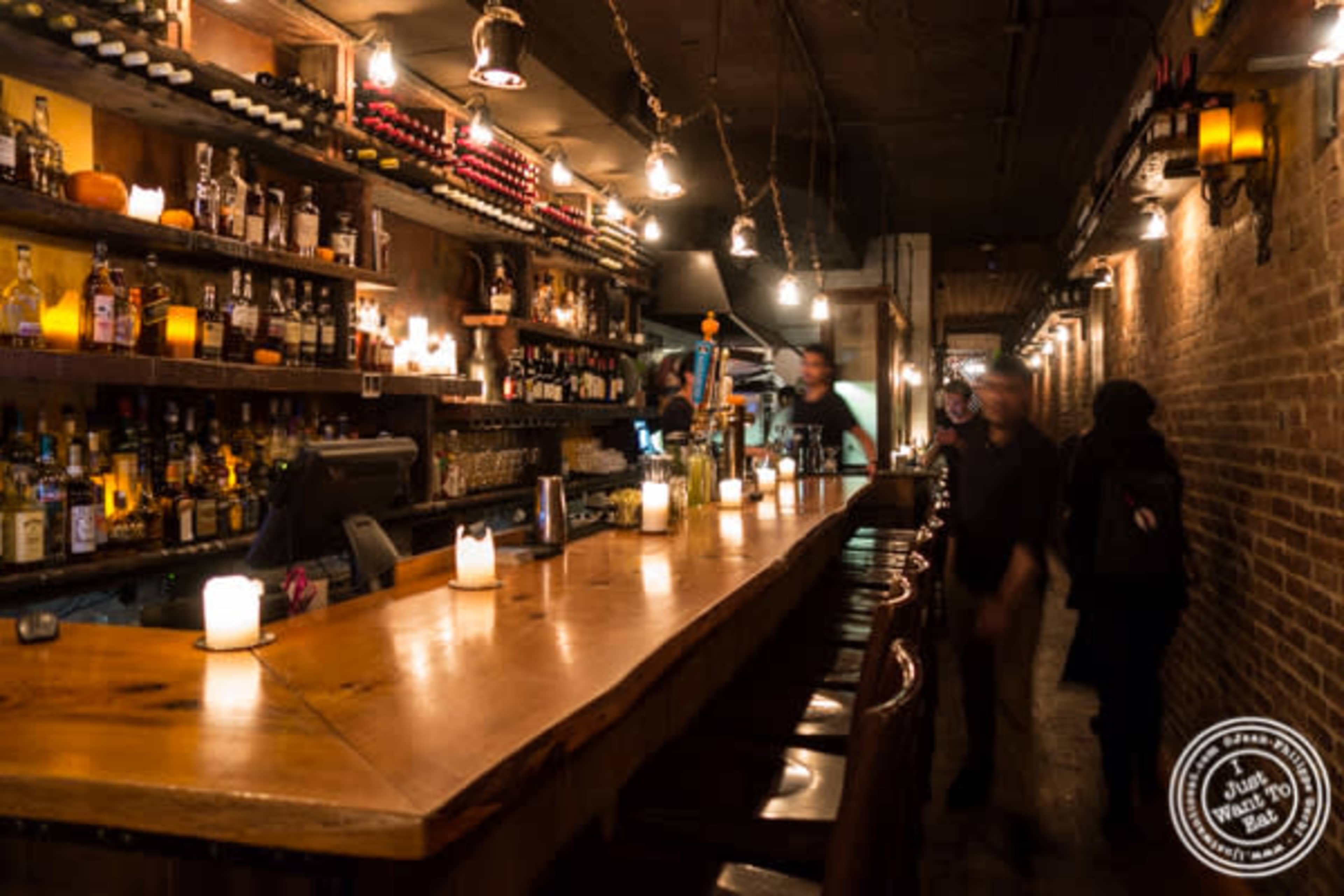 The image shows a dimly lit bar with bottles of liquor displayed on shelves behind a polished wooden counter.