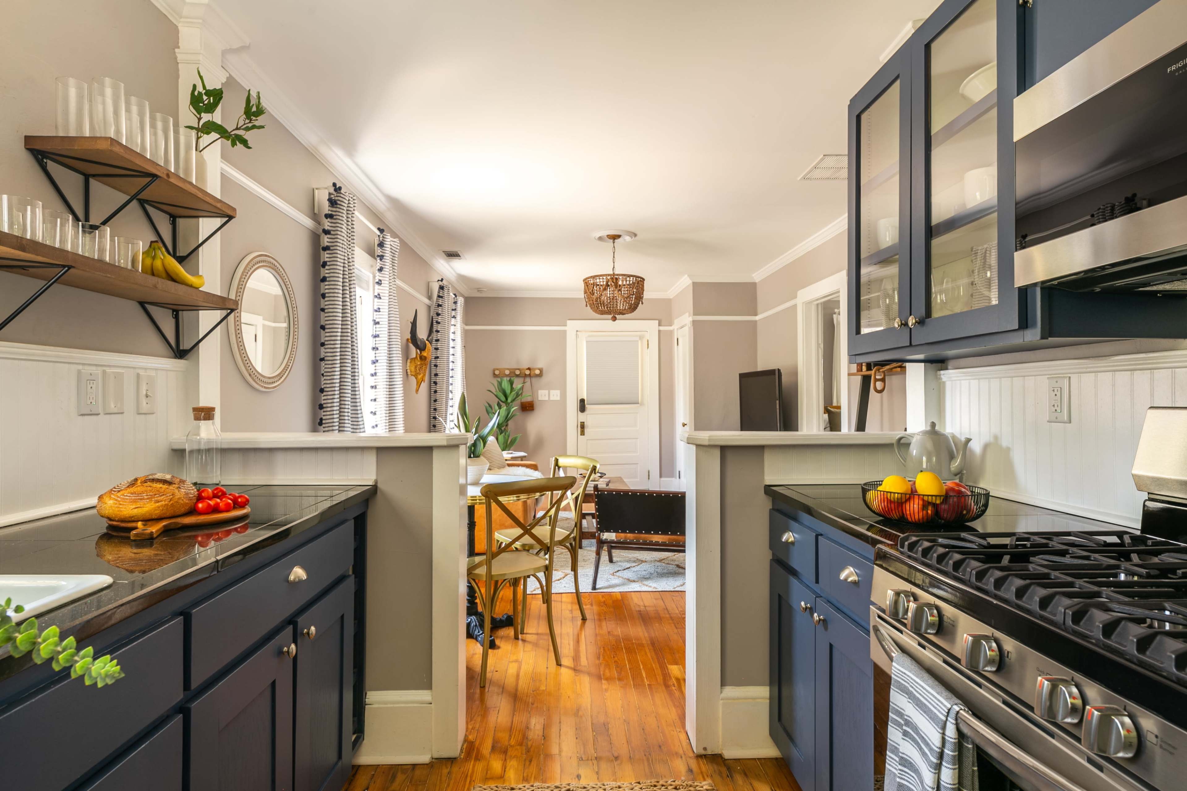A kitchen features dark blue cabinetry, a stainless steel stove, and a view into a dining area with wooden furniture and decorative elements.